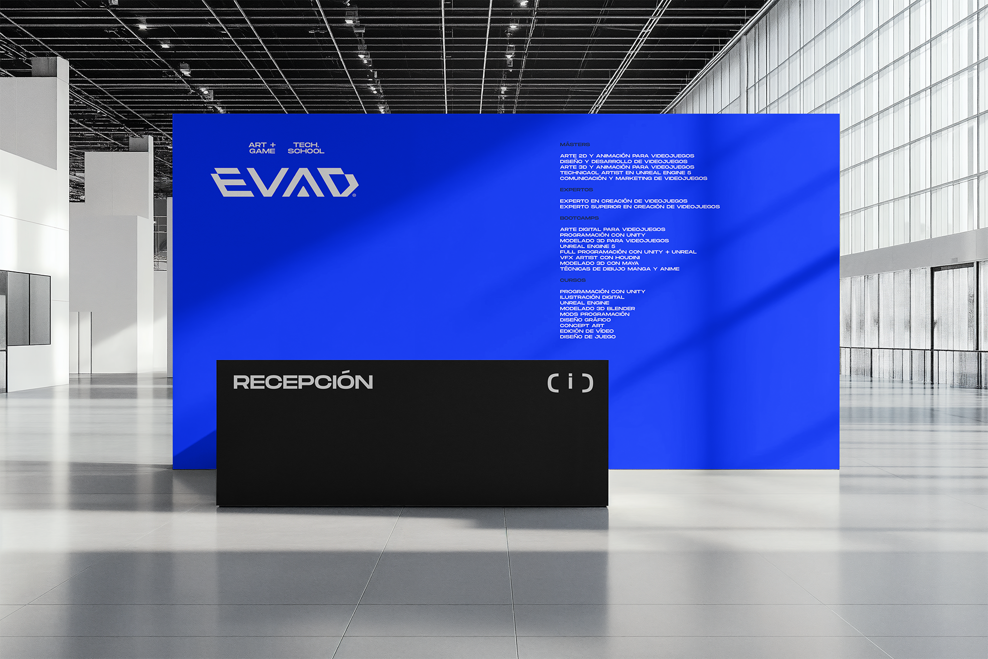 Pared azul en un centro de convenciones con información sobre cursos y programas de arte digital, videojuegos y tecnologías, y un área de recepción en primer plano.