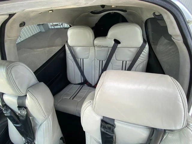 Interior view of a small aircraft with four light gray leather seats, labeled "Platinum," and seatbelts, showing spacious cabin design.