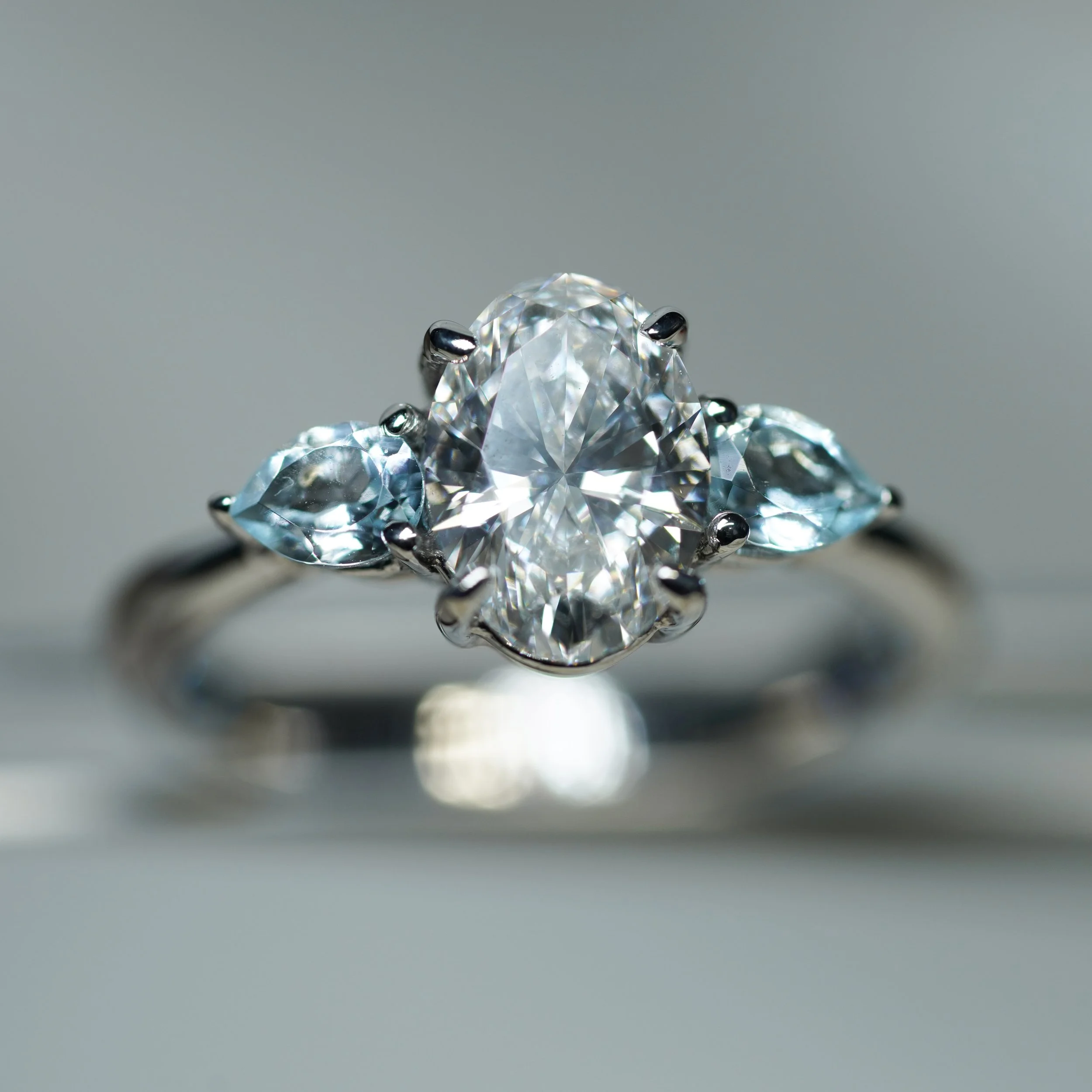 Anillo de compromiso en oro blanco con diamante central de corte oval de 1.00 ct con certificado gemológico y topacios naturales laterales de corte pera.