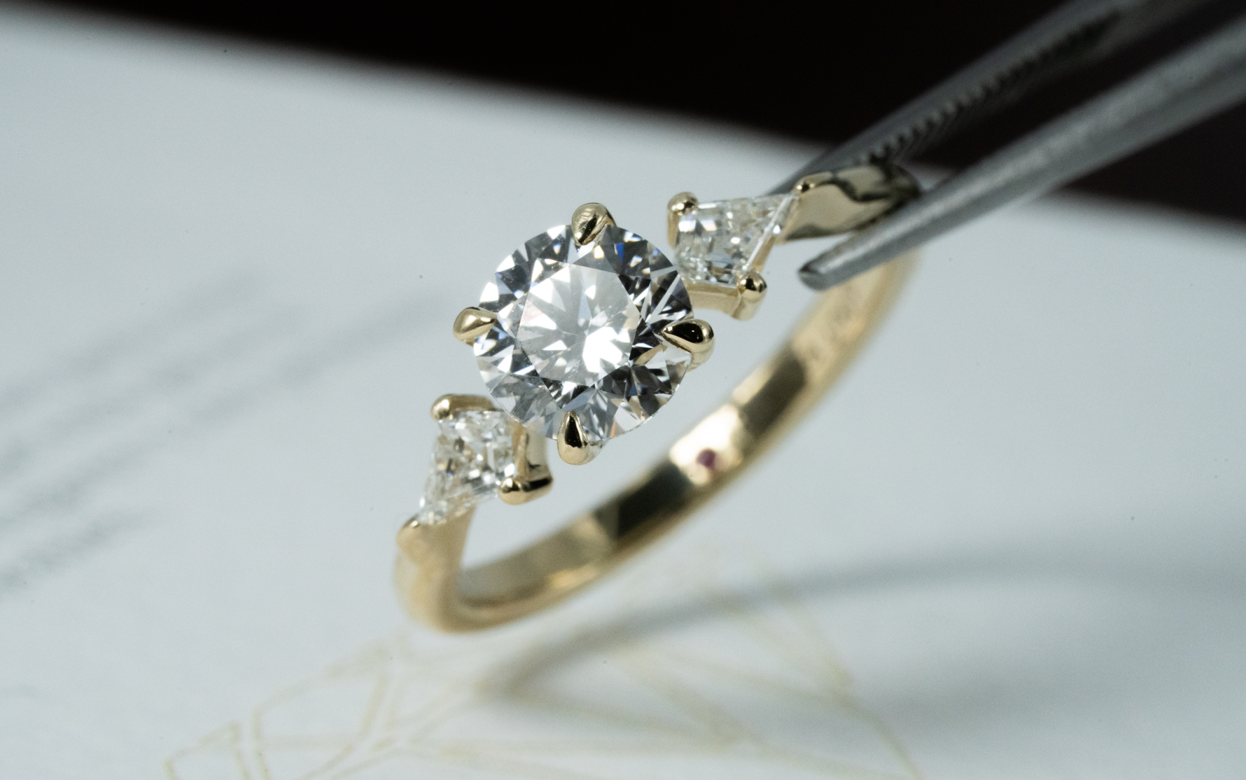 Anillo trilogía con diamante central de corte redondo y diamantes laterales de corte cometa, elaborado en oro amarillo.