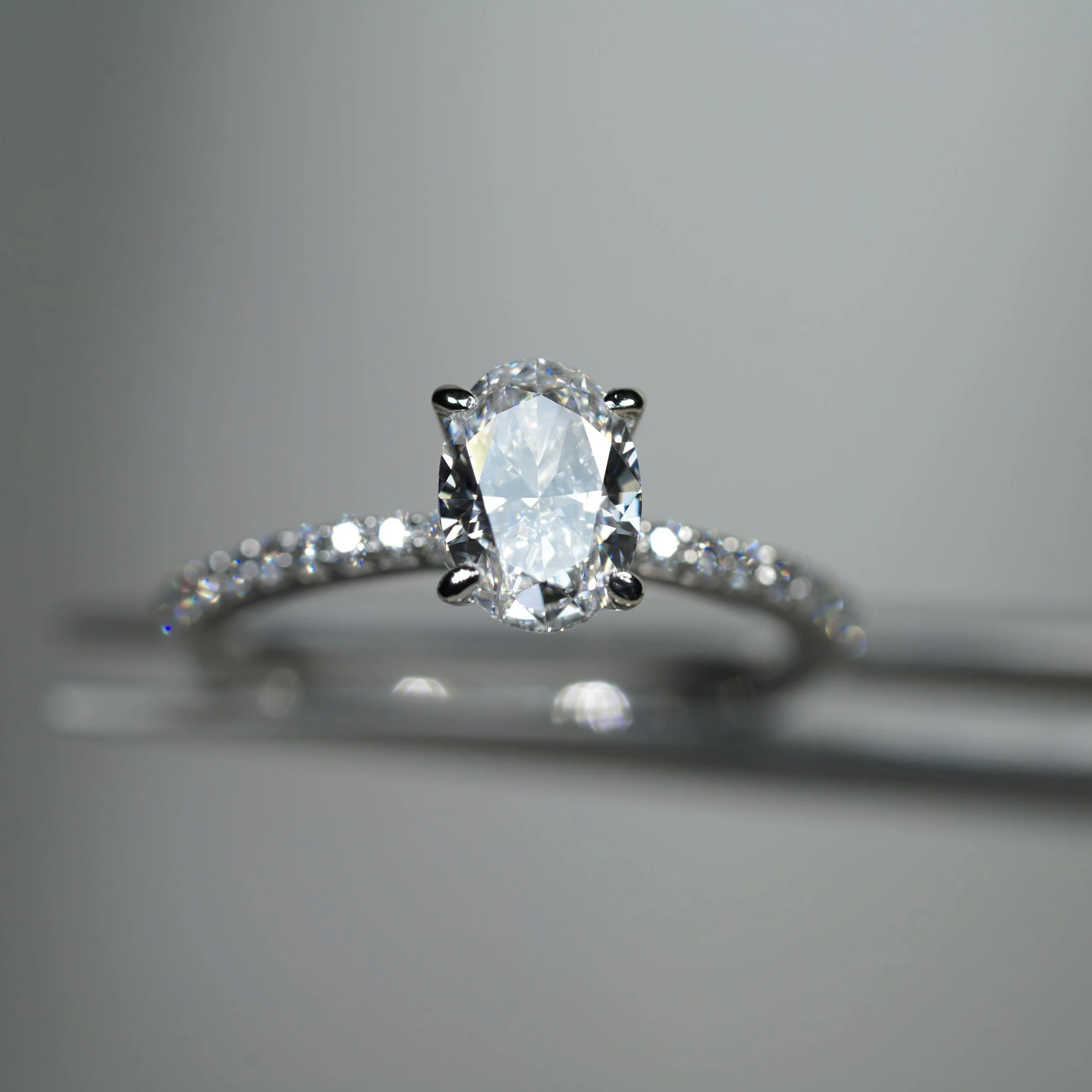 Anillo de compromiso en oro blanco con diamante central de corte oval y diamantes laterales engastados a lo largo de la banda.