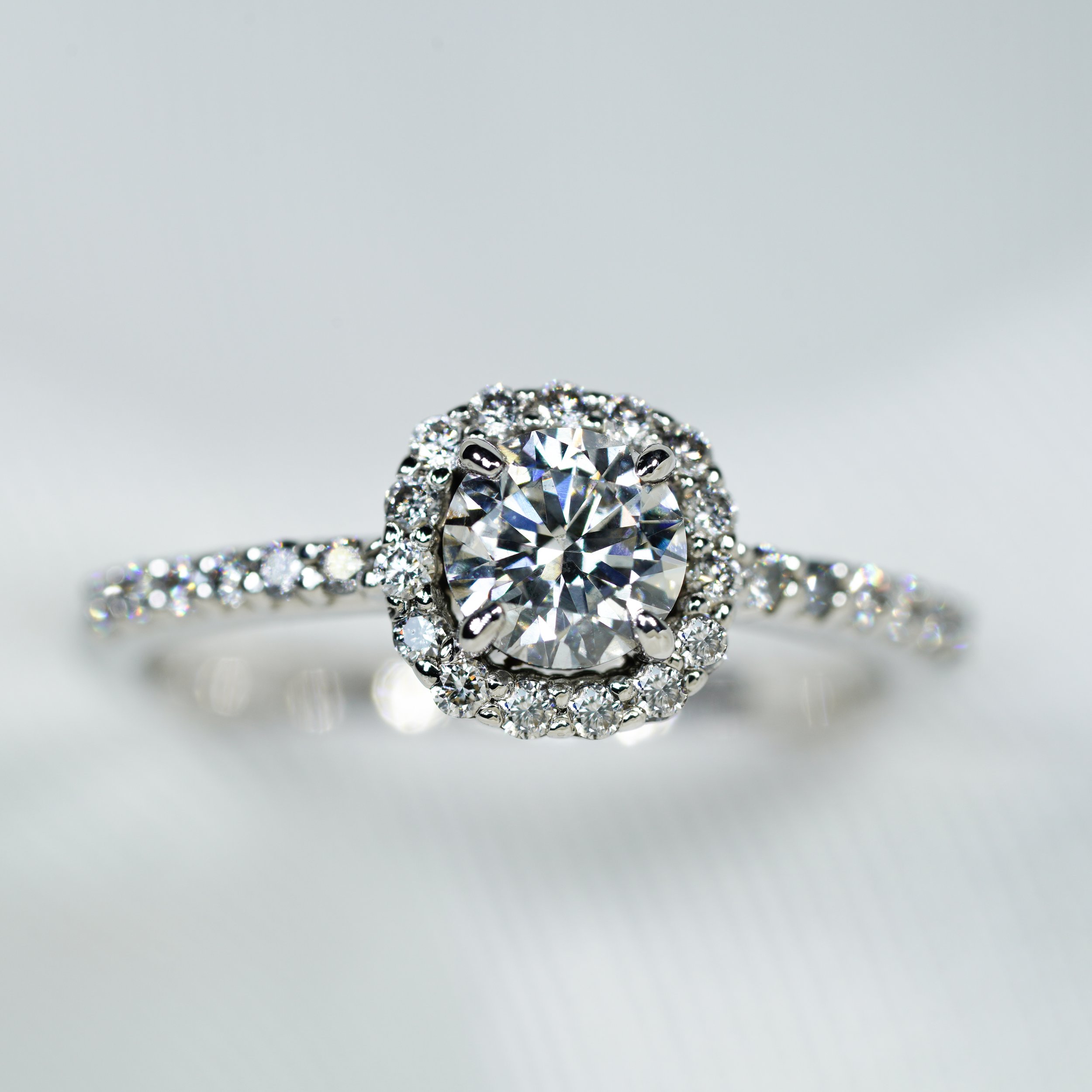 Anillo de compromiso en oro blanco con diamante central de corte brillante de 0.40 ct con certificado gemológico, halo de diamantes de corte brillante de 0.15 ct y diamantes laterales de corte brillante de 0.12 ct.