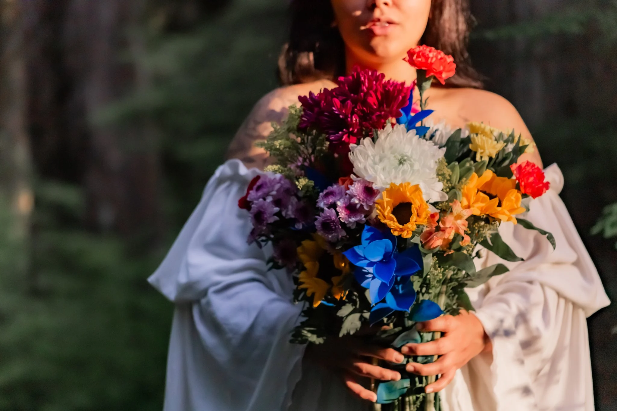 Person holding a large bouquet of colorful flowers including red, white, purple, yellow, and blue flowers, standing outdoors.