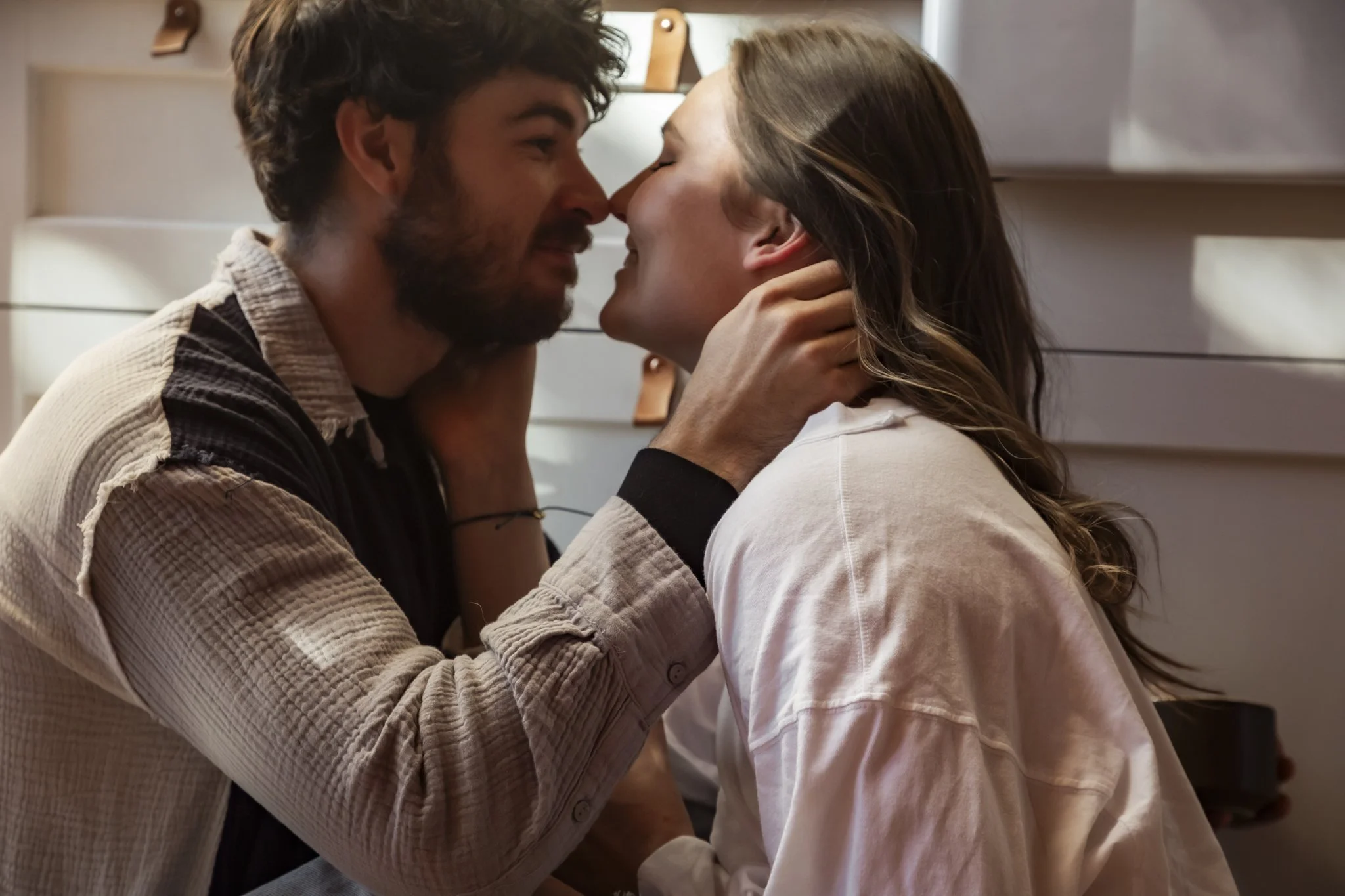 A young man and woman are in a close embrace, touching noses and smiling with their eyes closed, sharing an intimate moment.