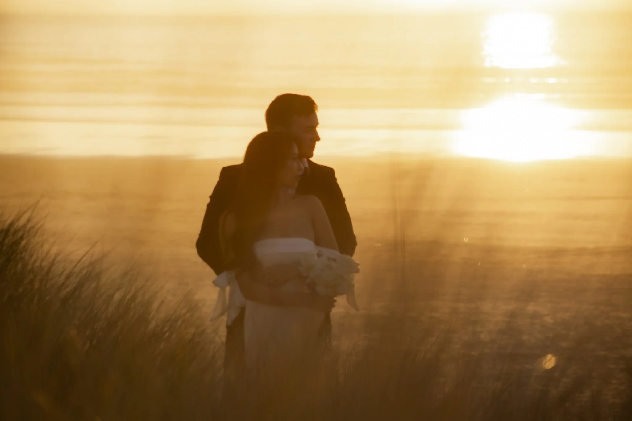A silhouette of a couple embracing by a body of water during sunset.