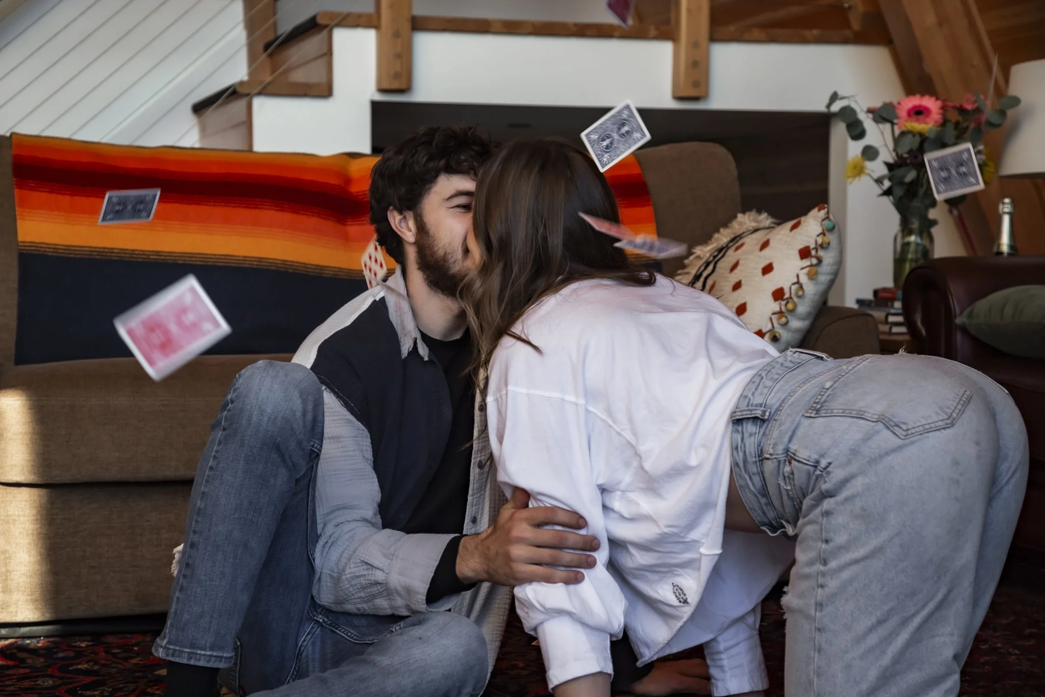 A man and woman sharing a kiss in a living room, with playing cards floating around them.