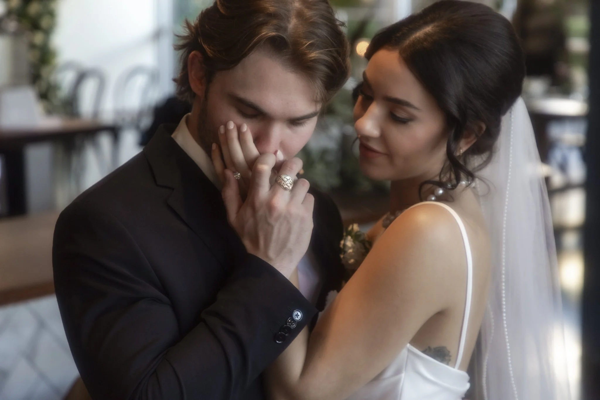 A man and woman share a close, intimate moment, with the man gently touching the woman's face as she looks at him affectionately, in a warmly lit indoor setting.