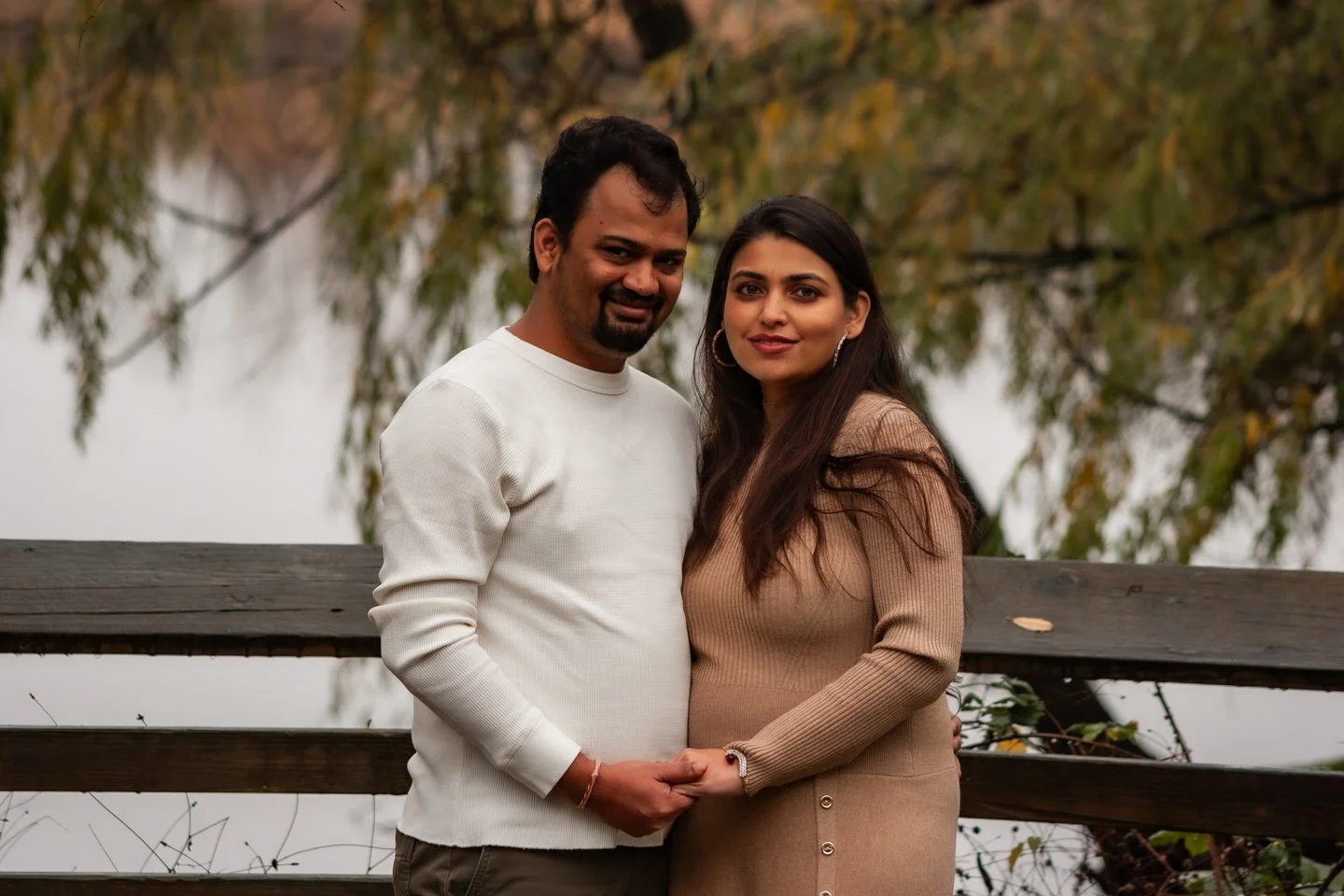 A couple holding hands outdoors on a wooden bridge, with trees in the background.