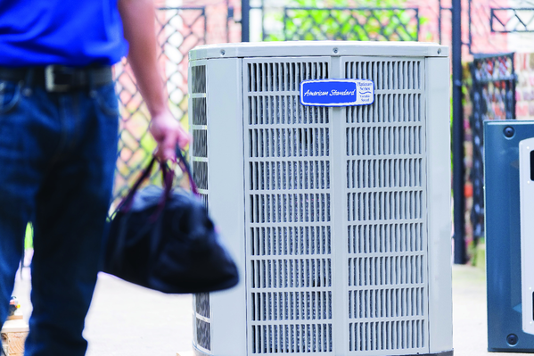 Close-up of a person carrying a black bag standing near a gray air conditioning unit outdoors.