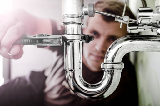 Person fixing or inspecting plumbing pipes under a sink.