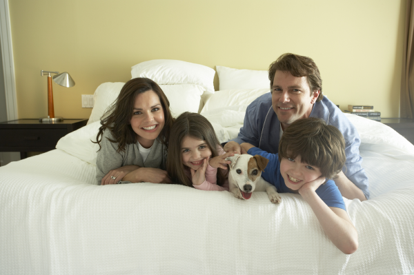 Family of four with a dog lying on a bed in a bedroom.