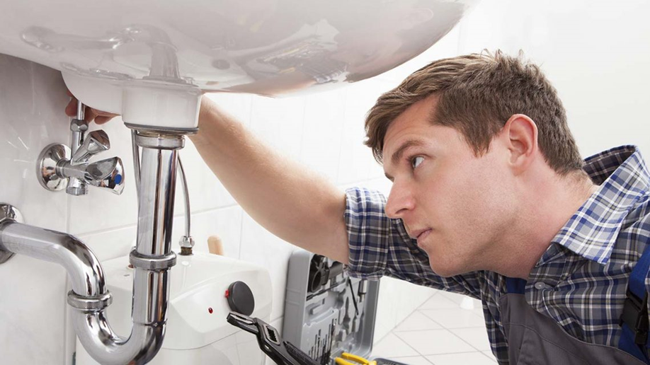 A plumber inspecting a sink's plumbing under a bathroom sink.