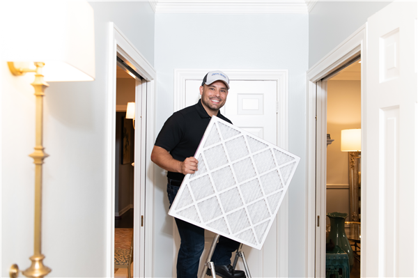 Man smiling while holding a large air filter in a hallway.