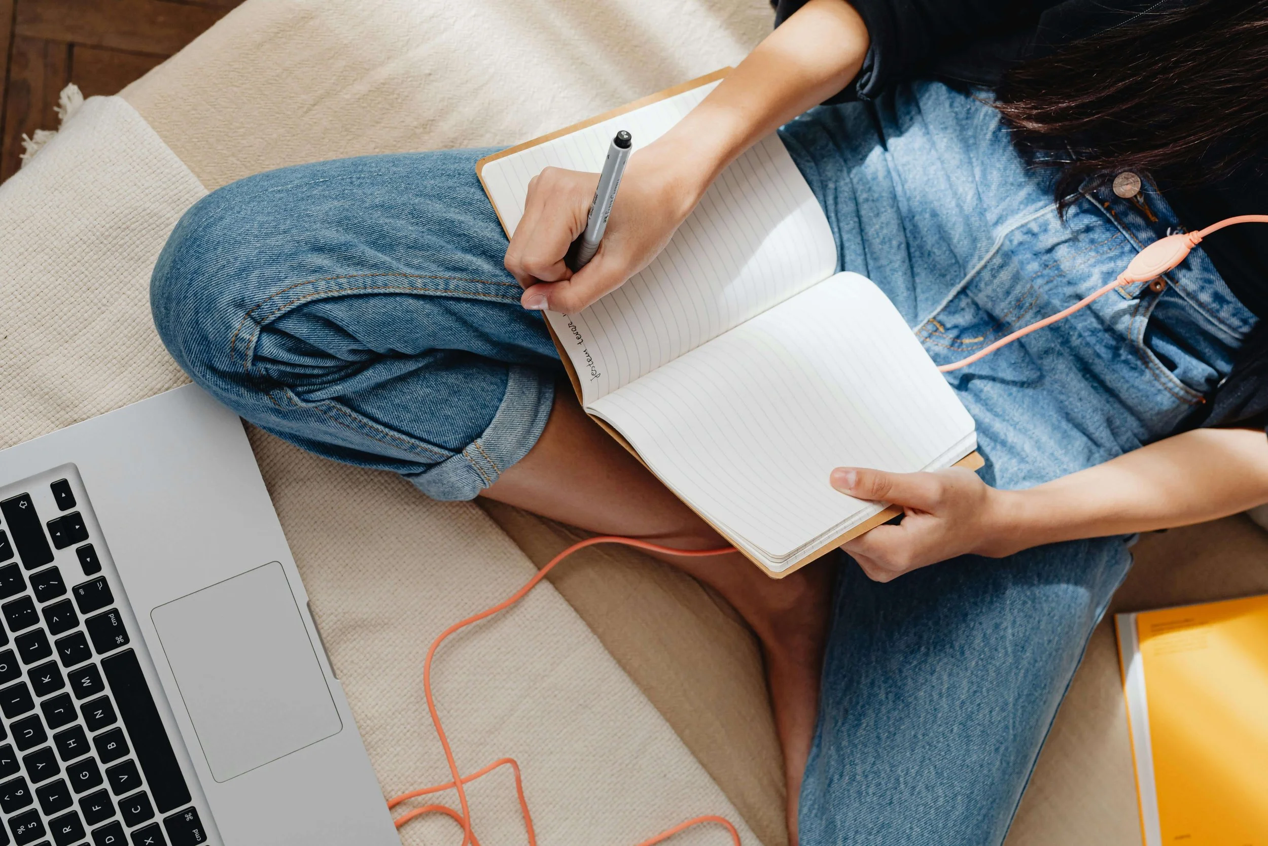 College student writing in notebook and sitting with laptop