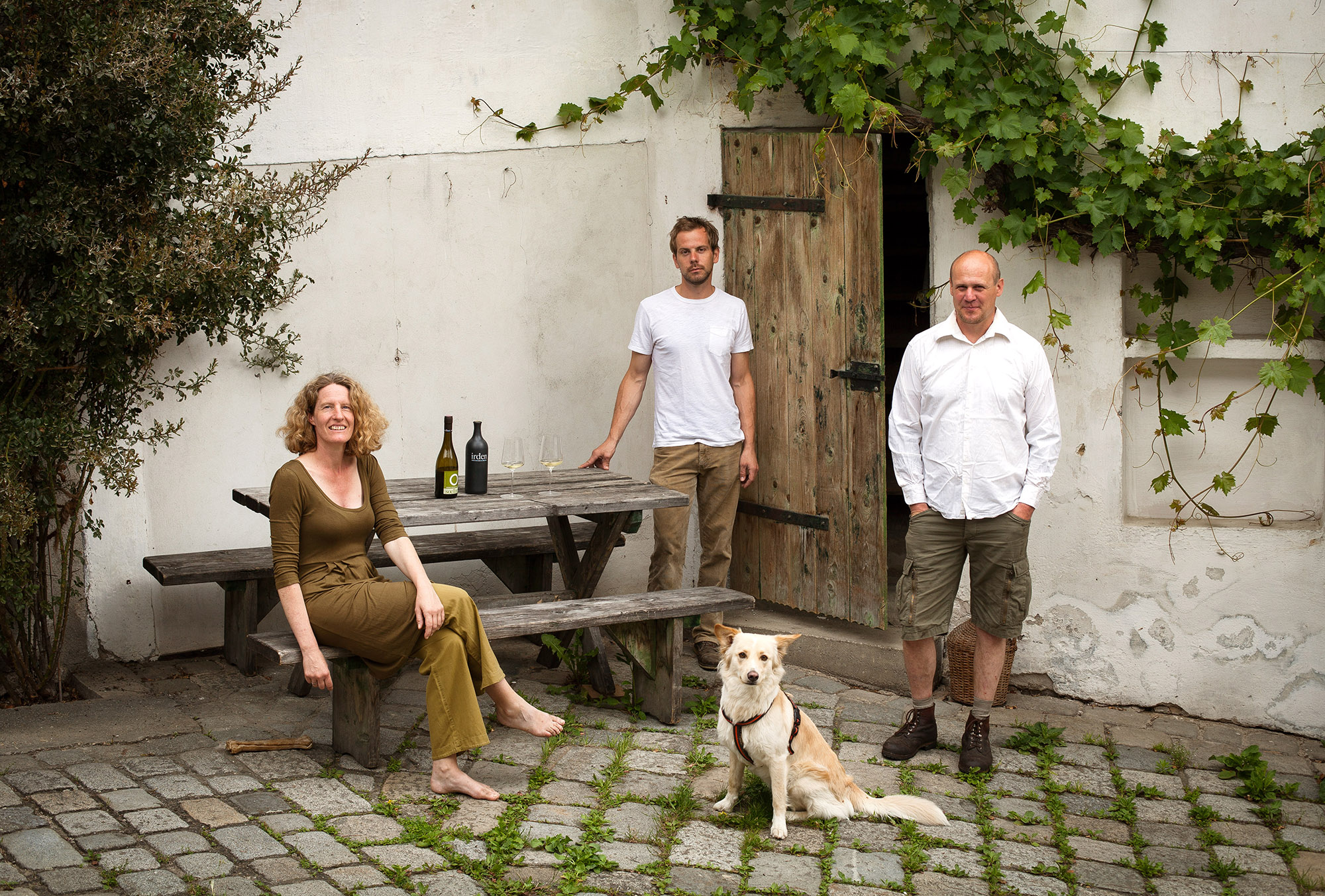 Toni and Daniela Soellner with a family member and their dog in the courtyard of Weingut Soellner, with bottles of their biodynamic Wagram wine on the picnic table — Gösing, Austria.