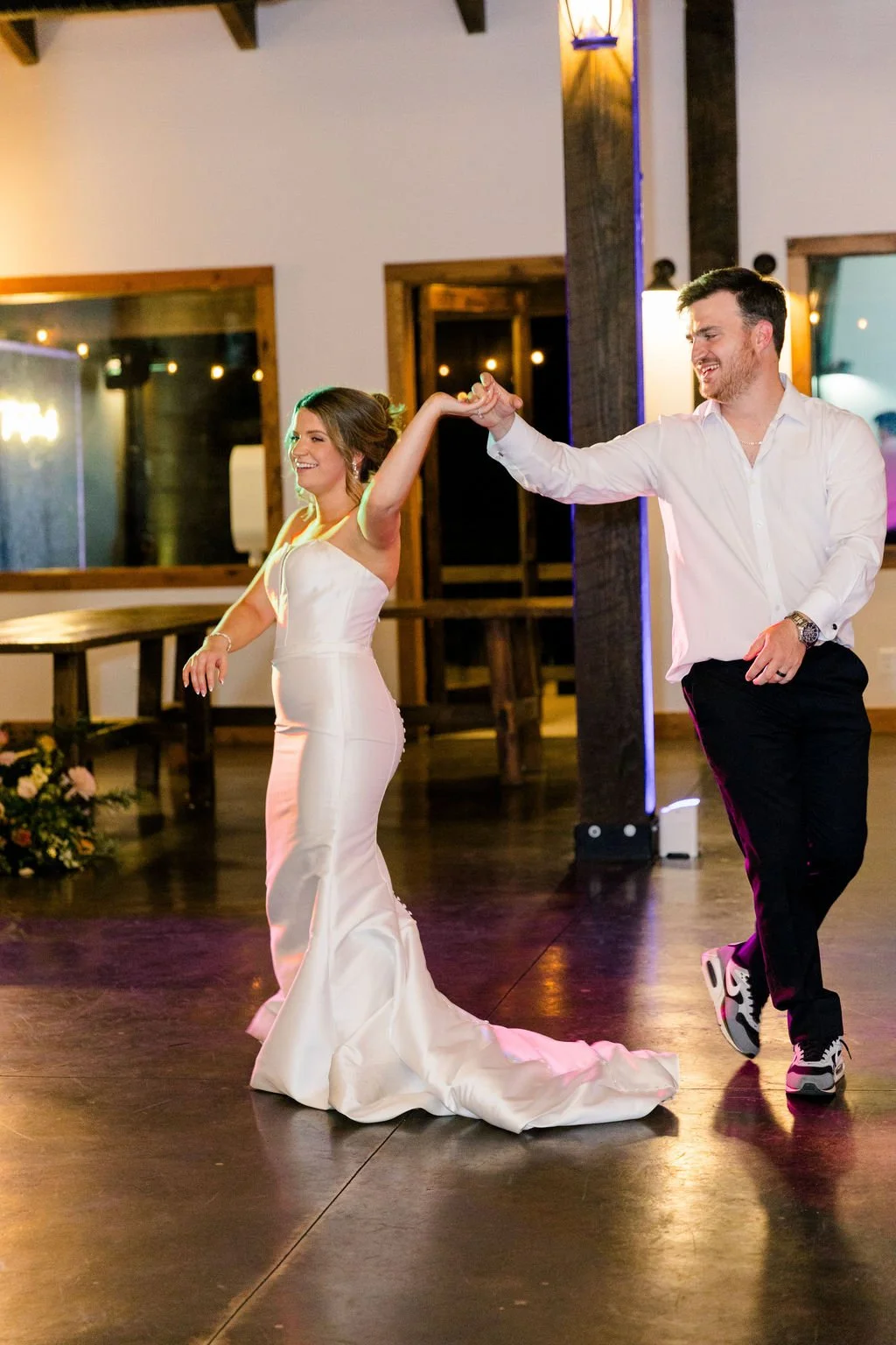 A bride and groom dance together at a wedding reception, holding hands and smiling.