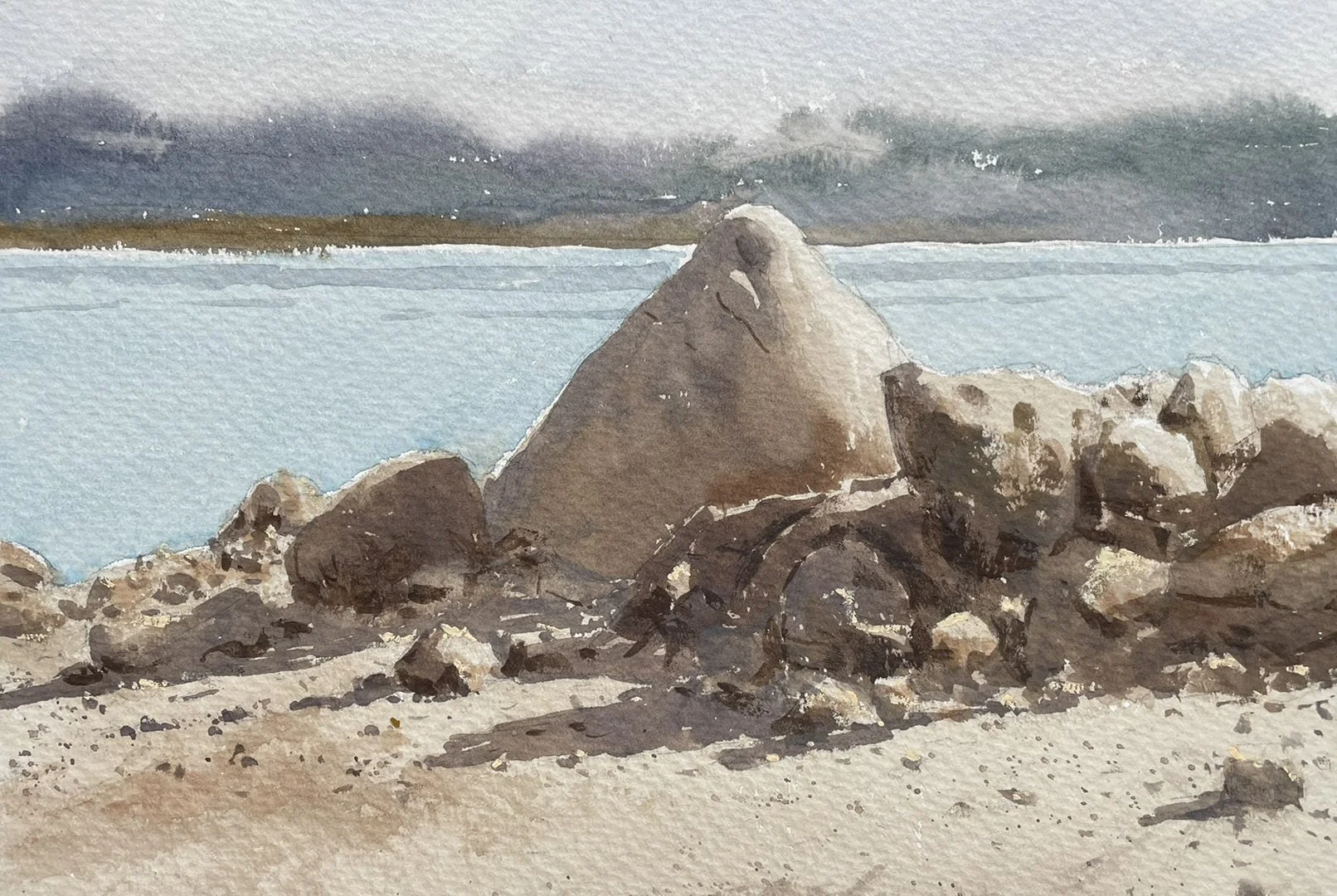Watercolor painting of a sandy shoreline with rocks and a large rock formation, ocean in the background, and cloudy sky