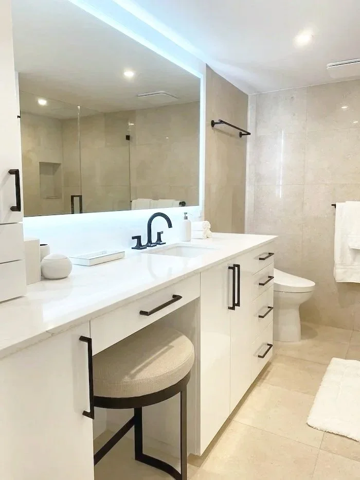 Modern bathroom with white vanity, large mirror, black fixtures, beige tiles, and a toilet.