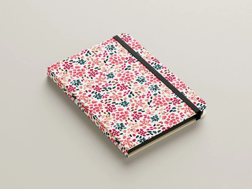 A closed floral patterned notebook with a black elastic band on a plain light-colored surface.