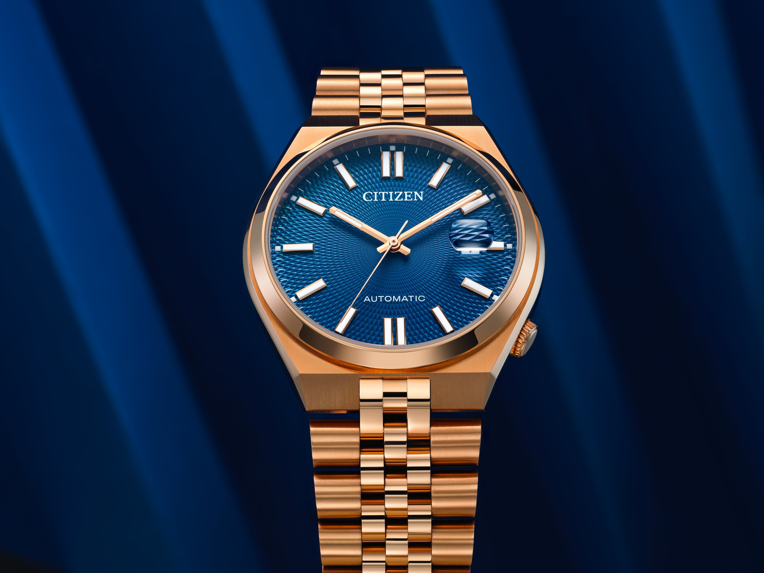 A Citizen automatic wristwatch with a gold band and case, and a blue textured dial with gold markers and hands, set against a dark blue background.