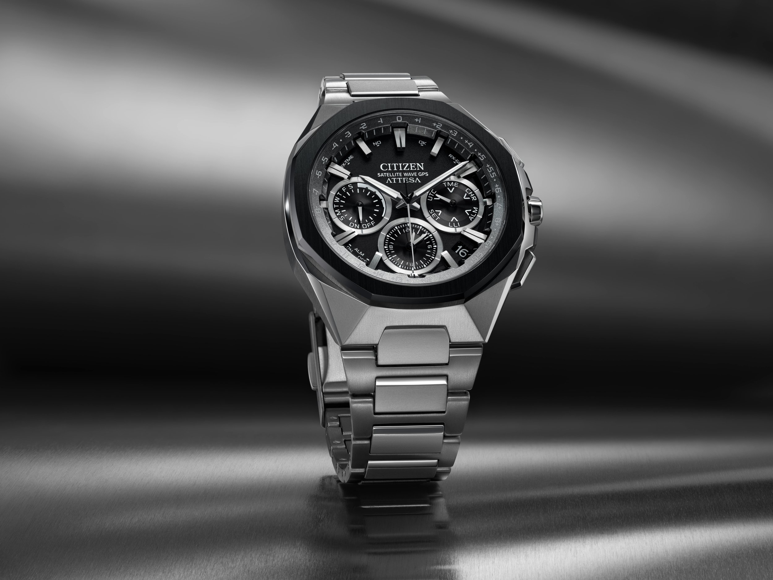 A silver Citizen Attesa satellite wave GPS wristwatch with a black dial, multiple subdials, and a stainless steel band, displayed on a metallic surface with a blurred dark background.