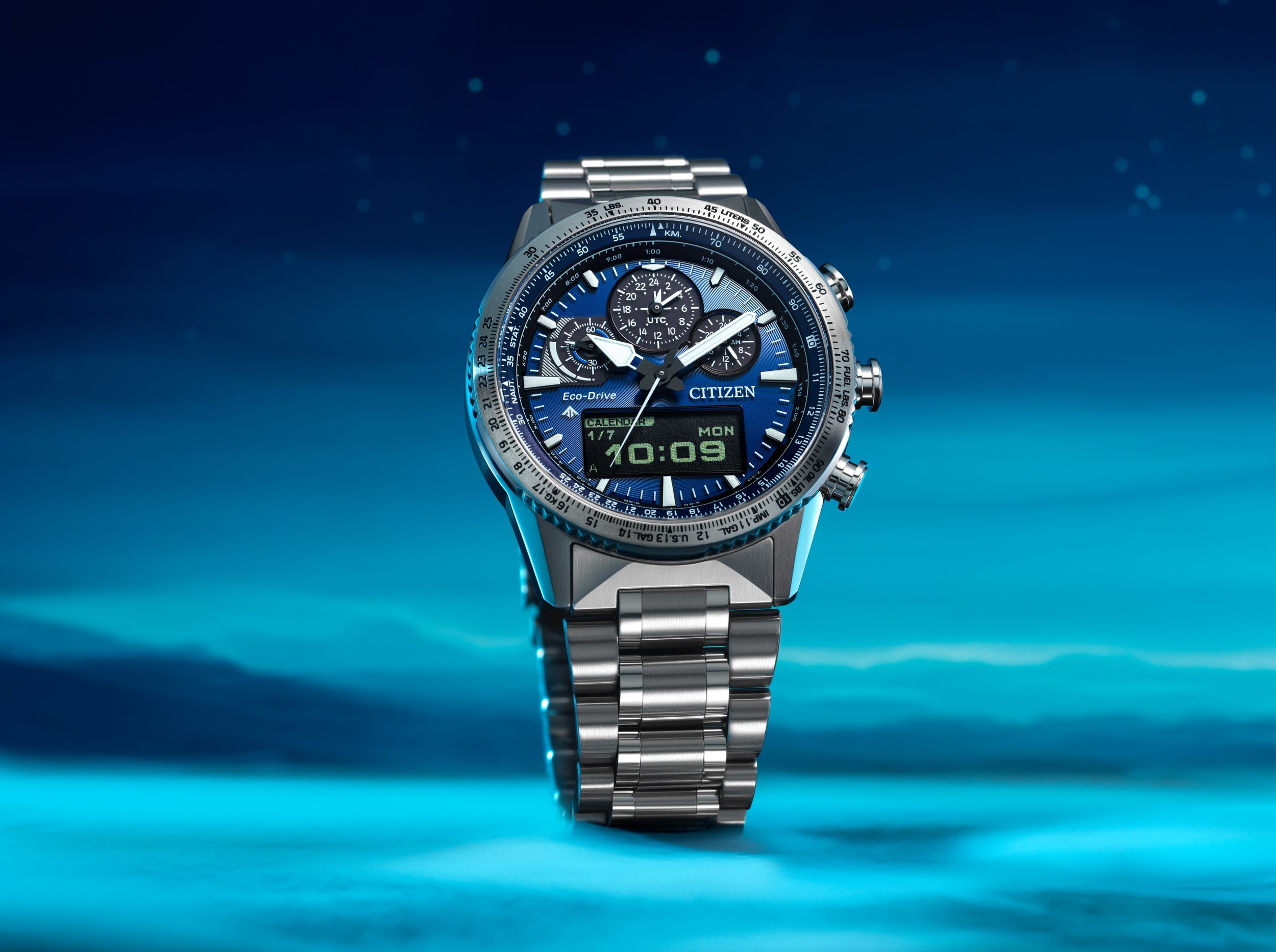 A silver Citizen Eco-Drive wristwatch with a blue dial, multiple chronograph sub-dials, and a digital display showing the time 10:09 on a blue gradient background with light streaks.
