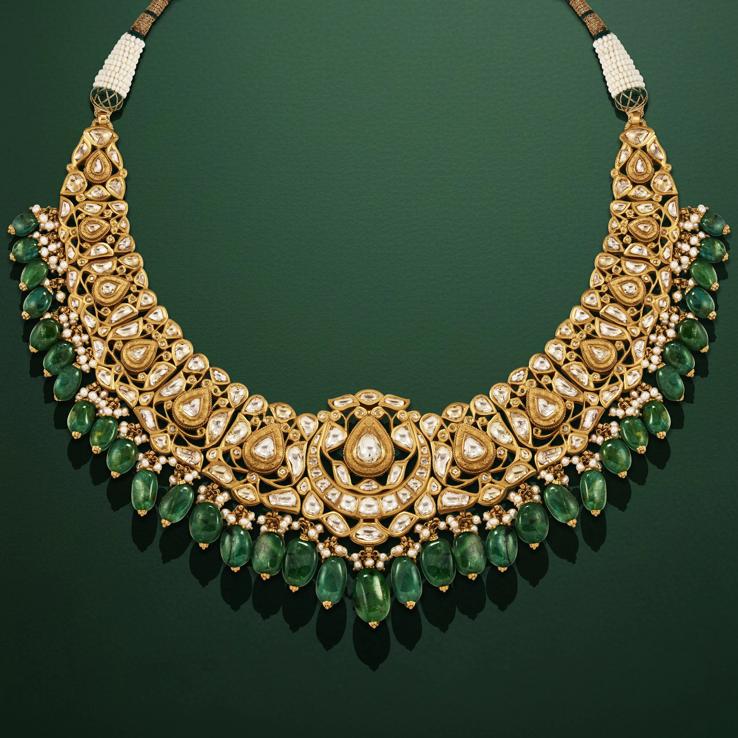 A gold necklace with intricate designs, featuring white and green gemstones, displayed on a green background.