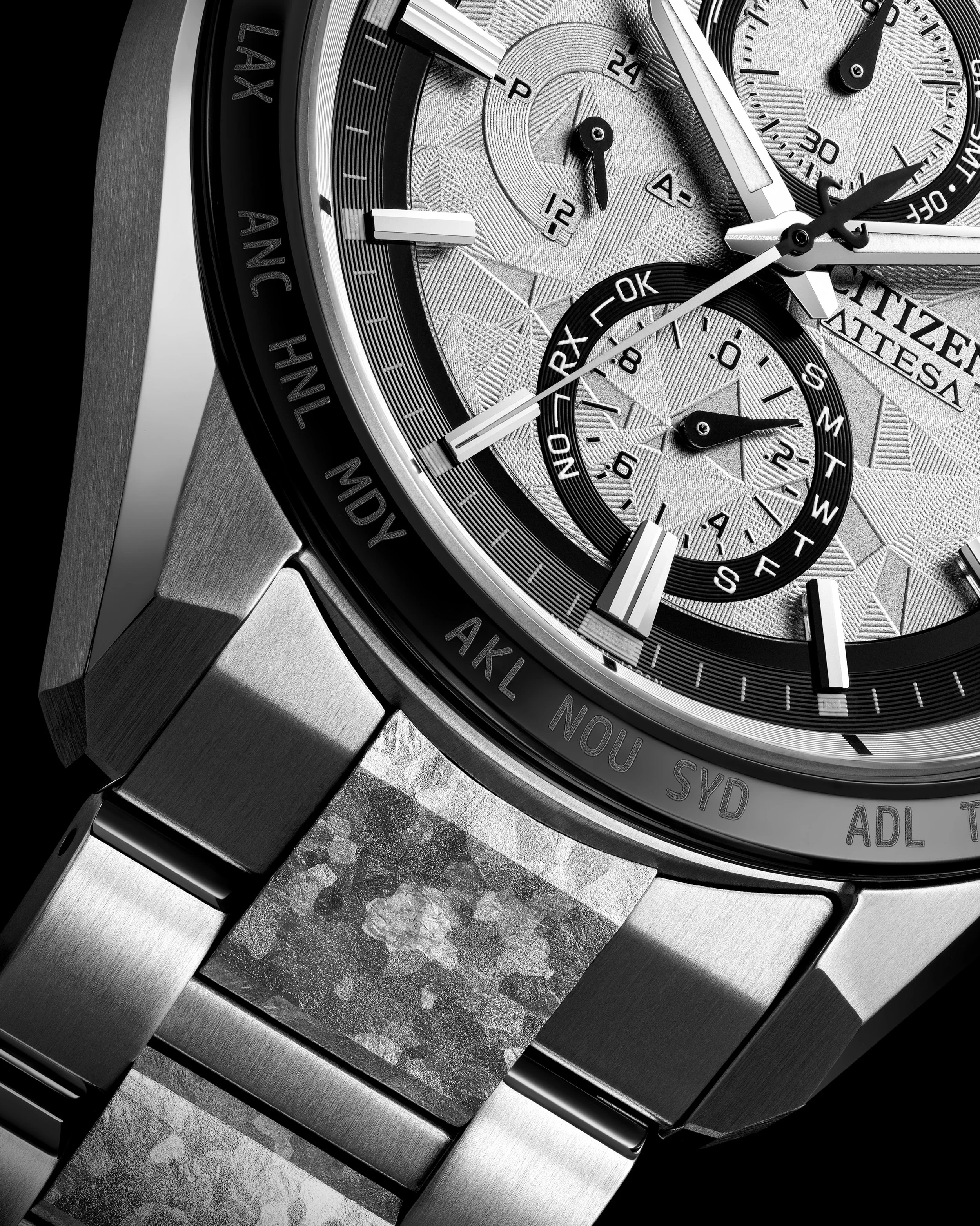 Close-up of a silver Citizen wristwatch with multiple dials, buttons, and a world time bezel showing city abbreviations.