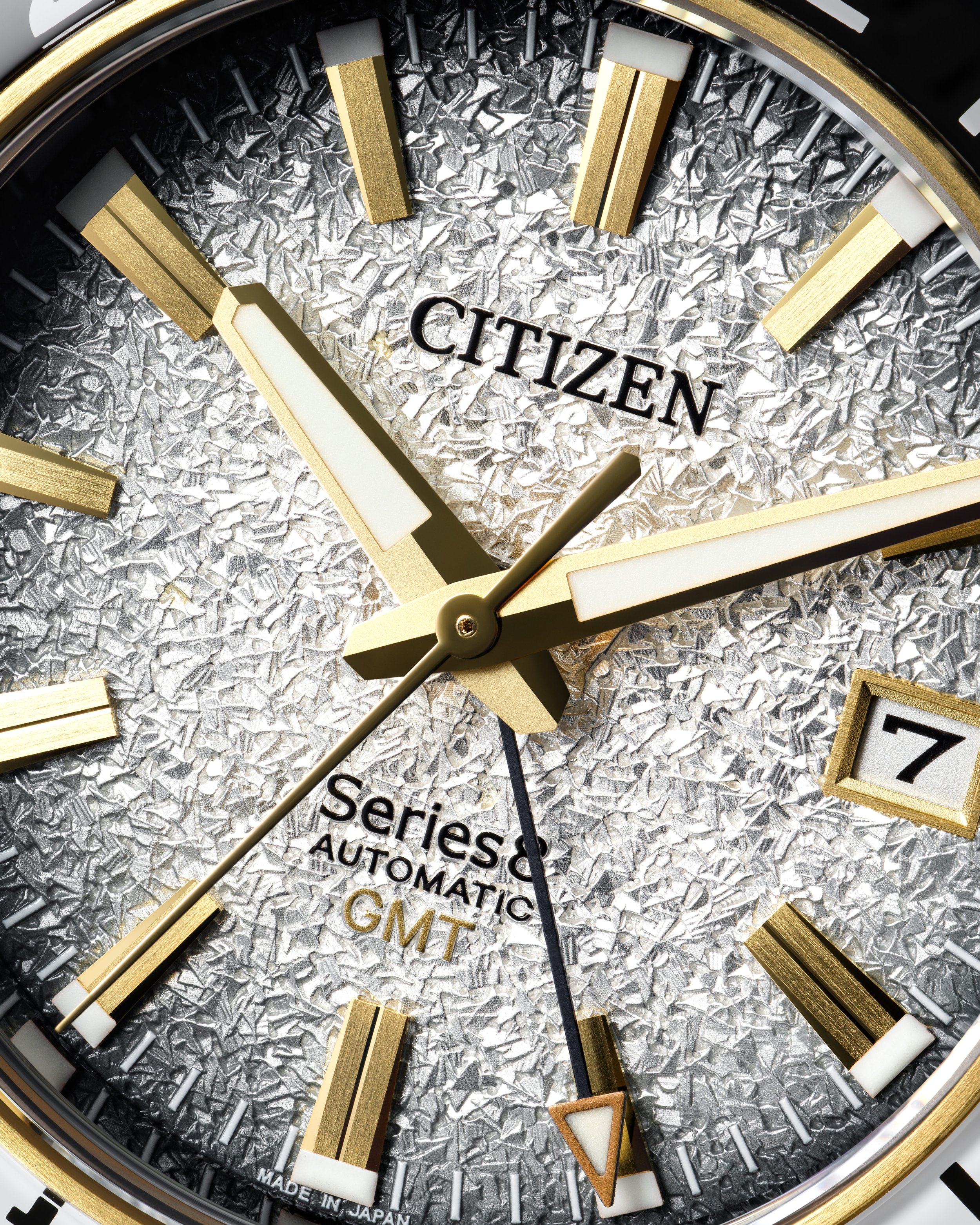 Close-up of Citizen watch face with gold markers, textured silver background, and date display showing 7. The watch has gold hour, minute, and second hands.