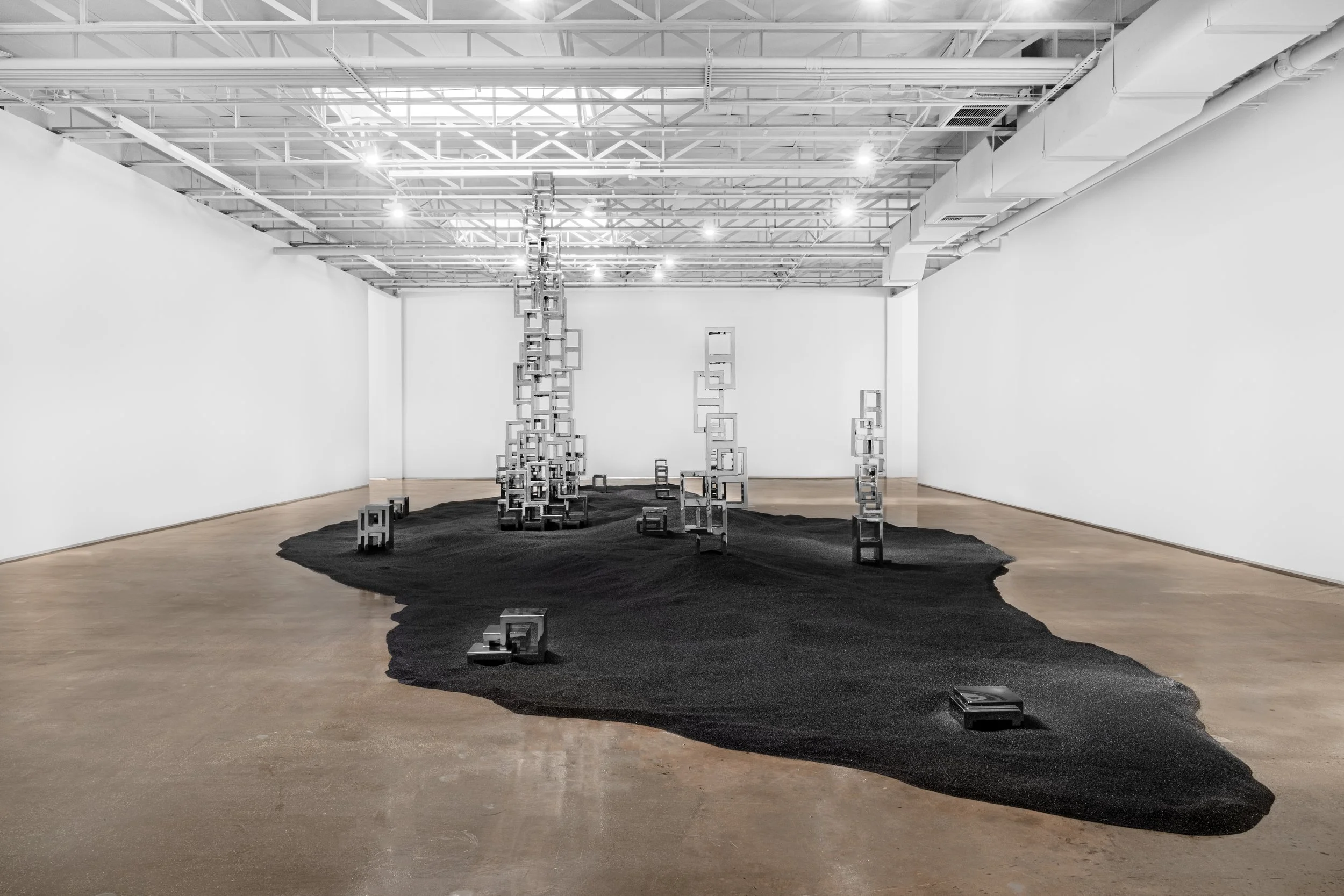 An art installation consisting of hanging beer bottles suspended by colorful ropes in an art gallery, with crumpled paper on the floor and a white artwork on the wall.