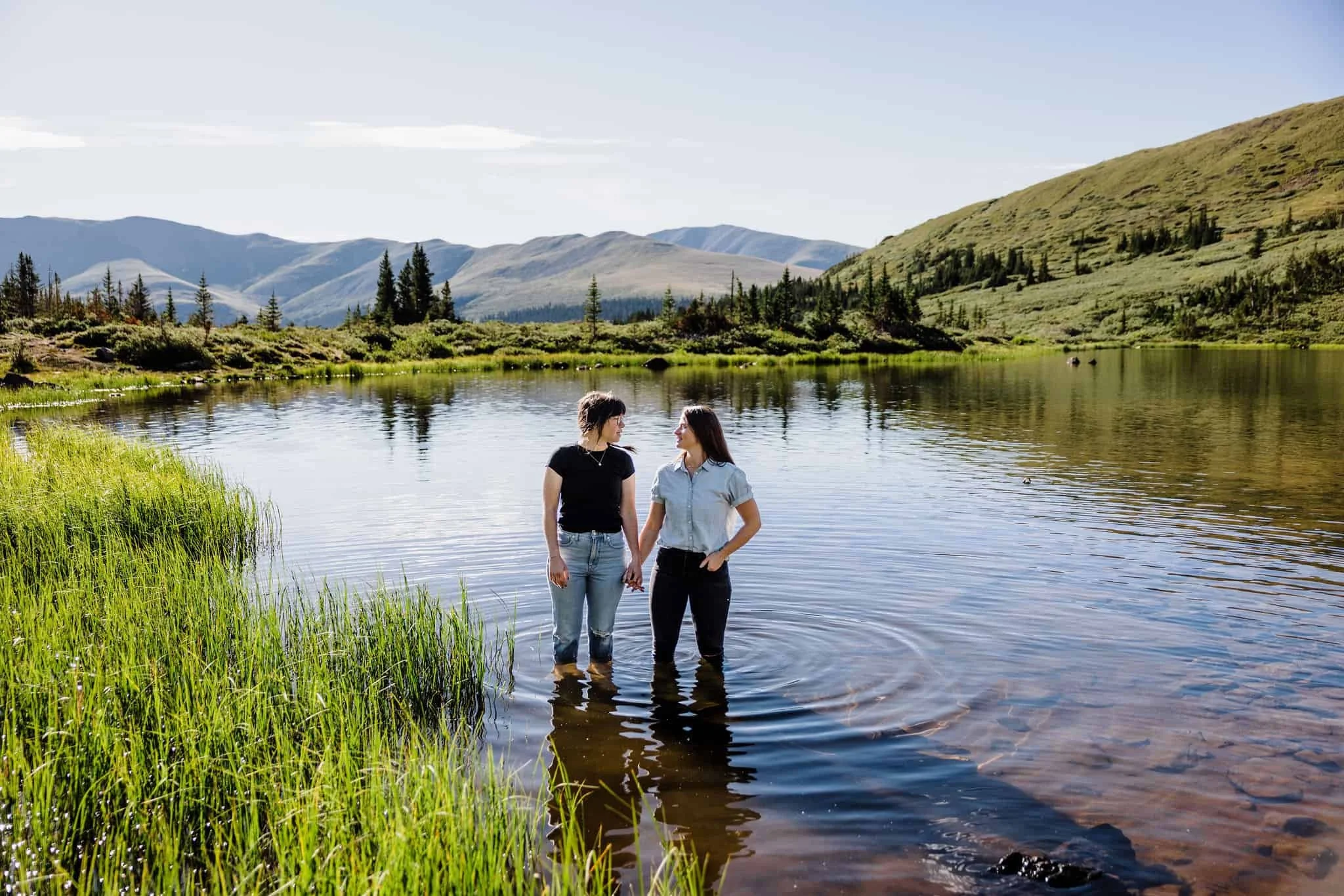A couple holds hands while standing in an alpine lake