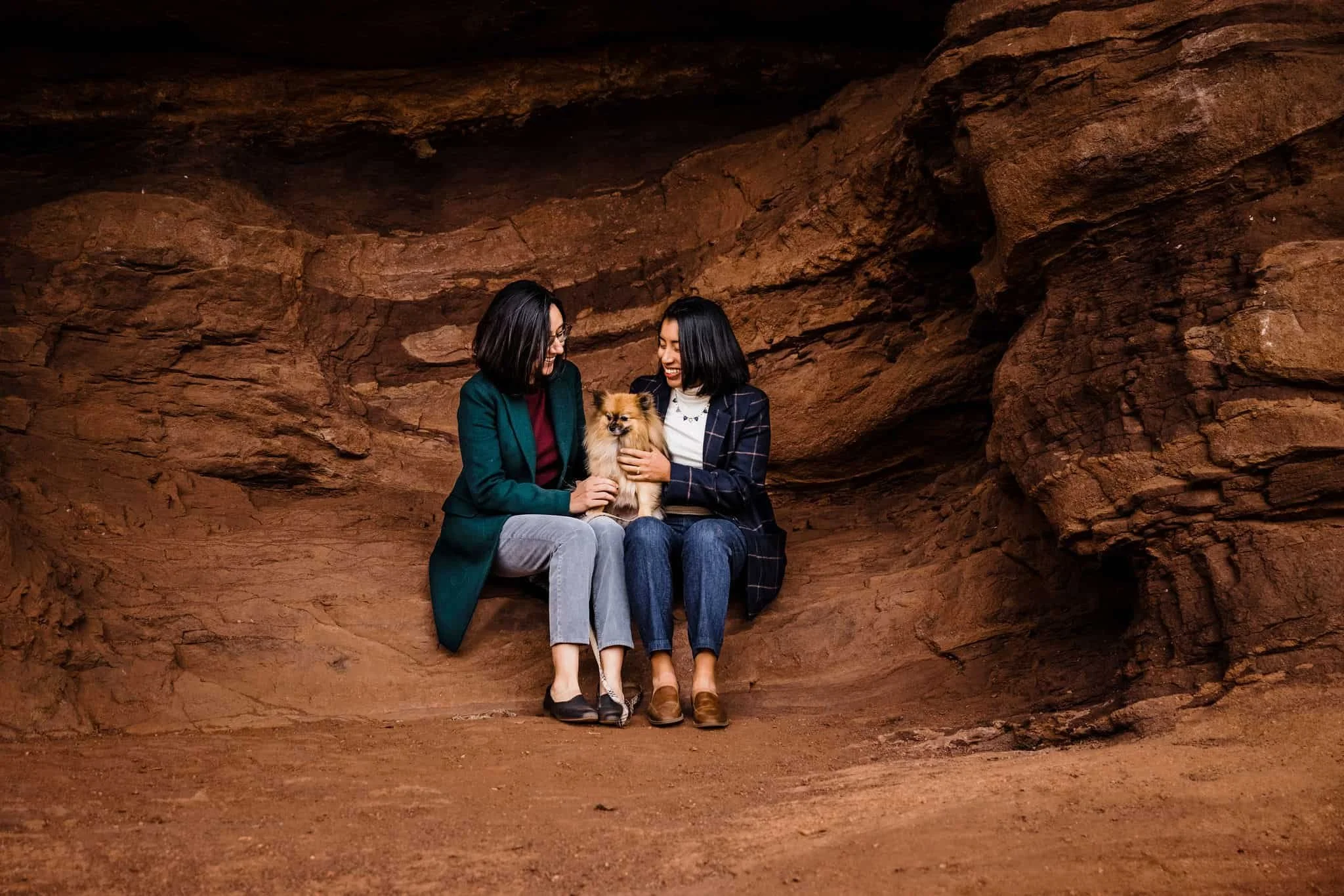 A couple sits on a rock with their small dog