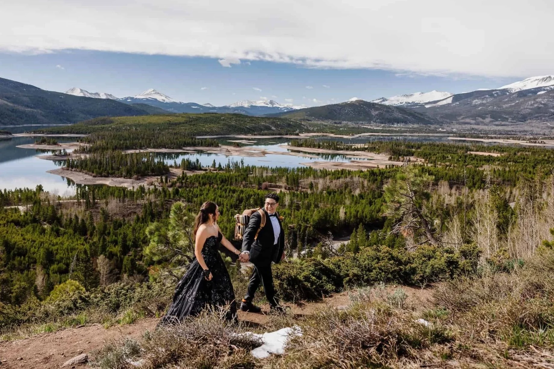 A couple holds hands while hiking above a mountain lake
