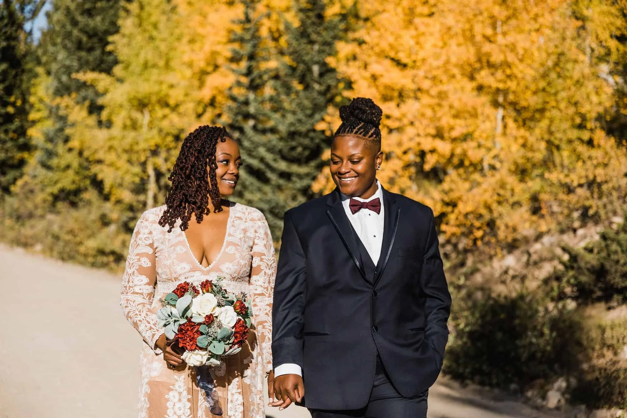 Two brides walk with fall color in the background