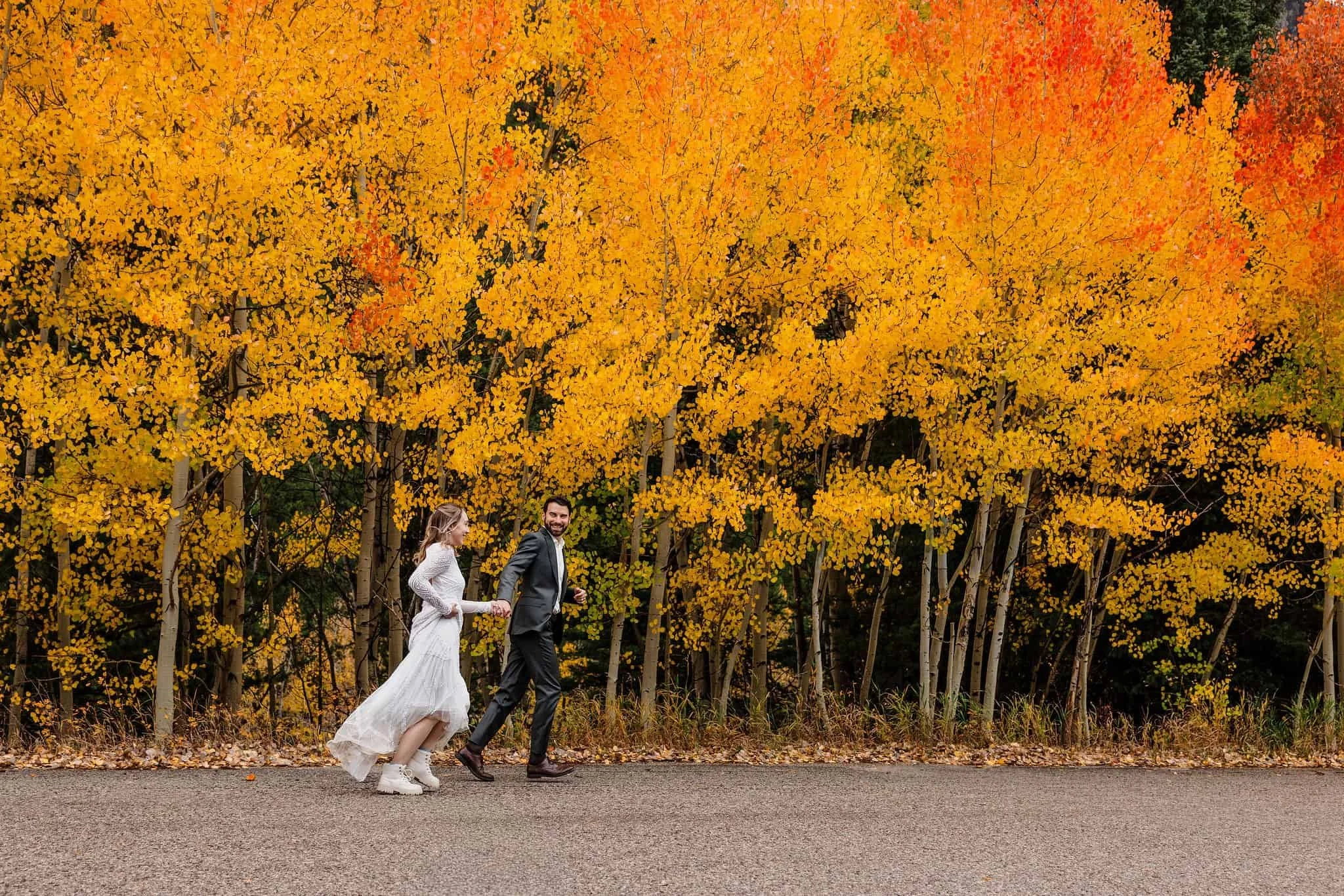 A couple runs through yellow and orange aspen trees