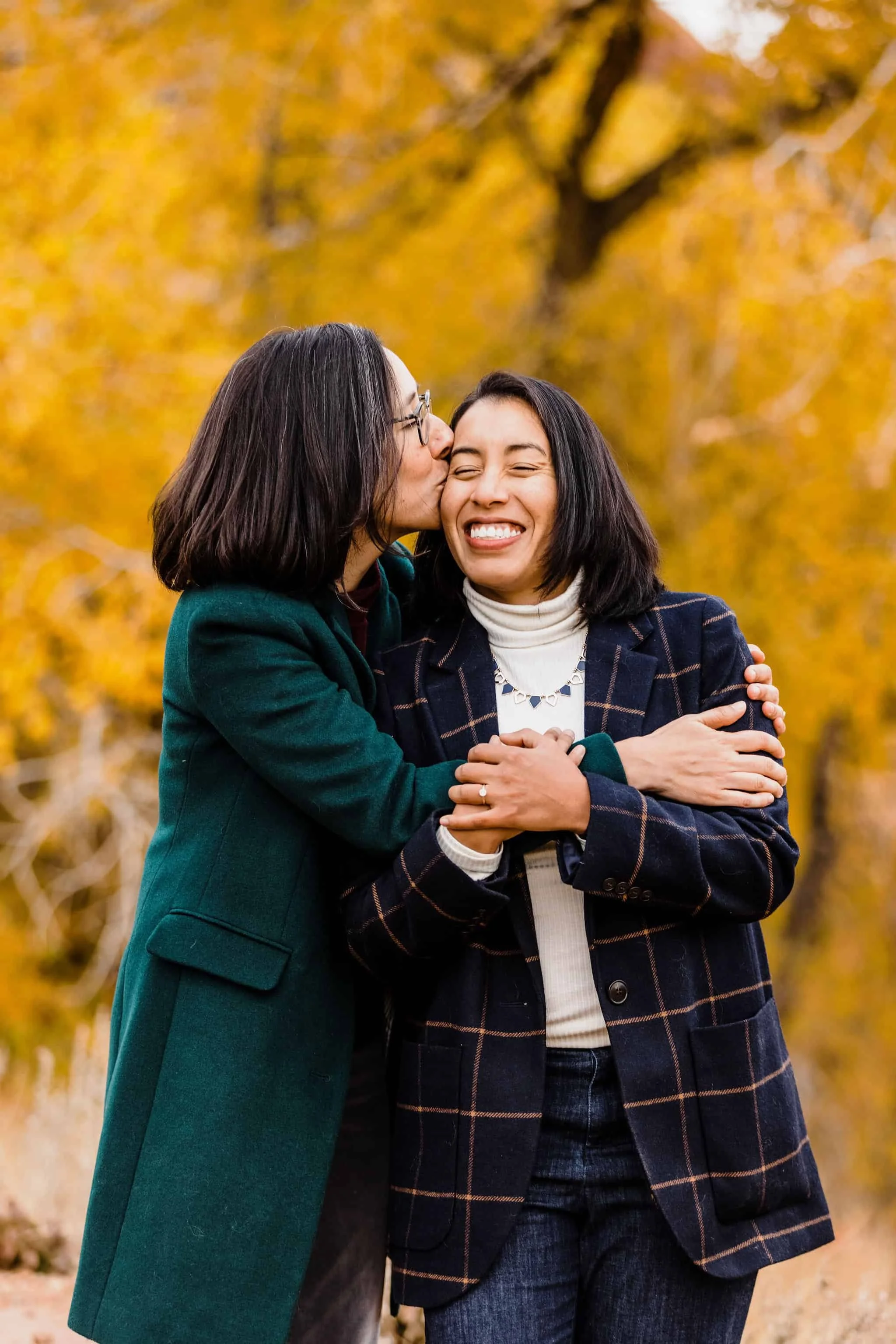 A couple cuddle each other in front of yellow leaves