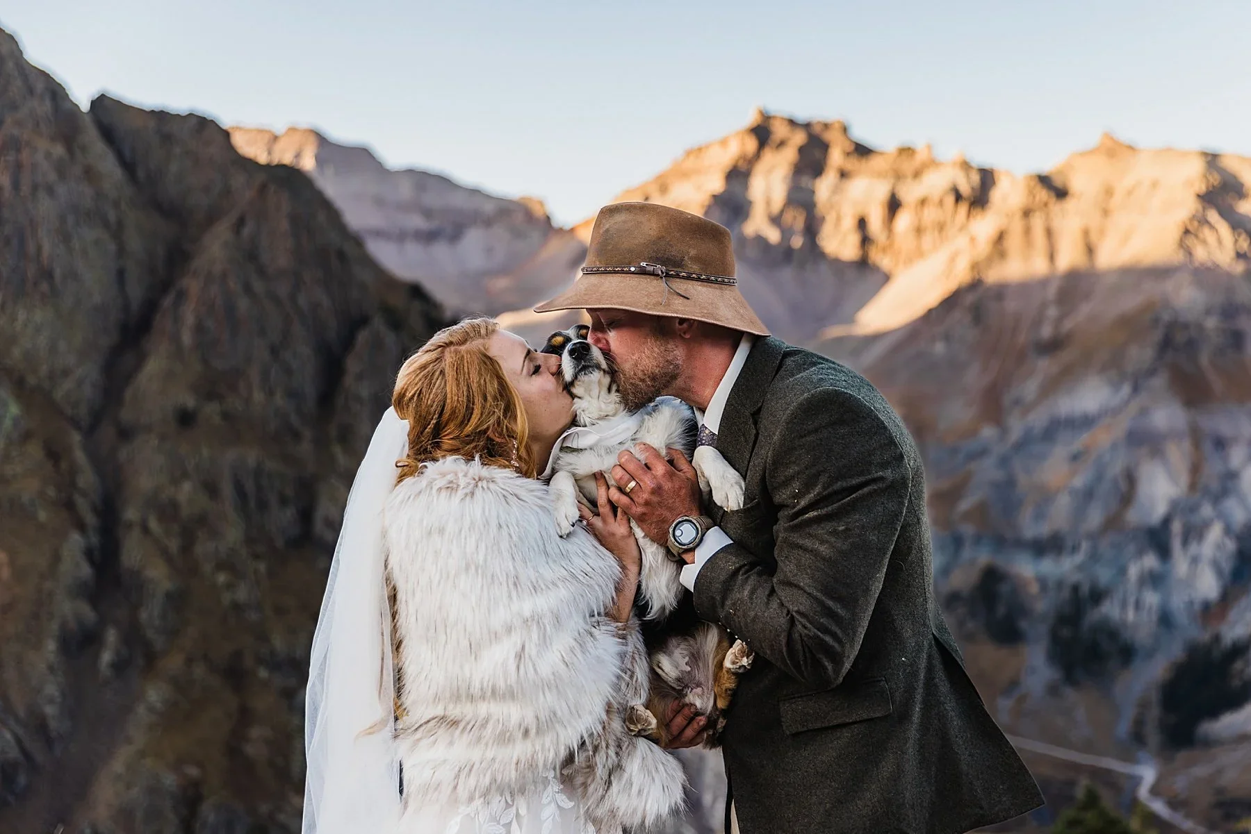 A couple kisses their dog in the mountains