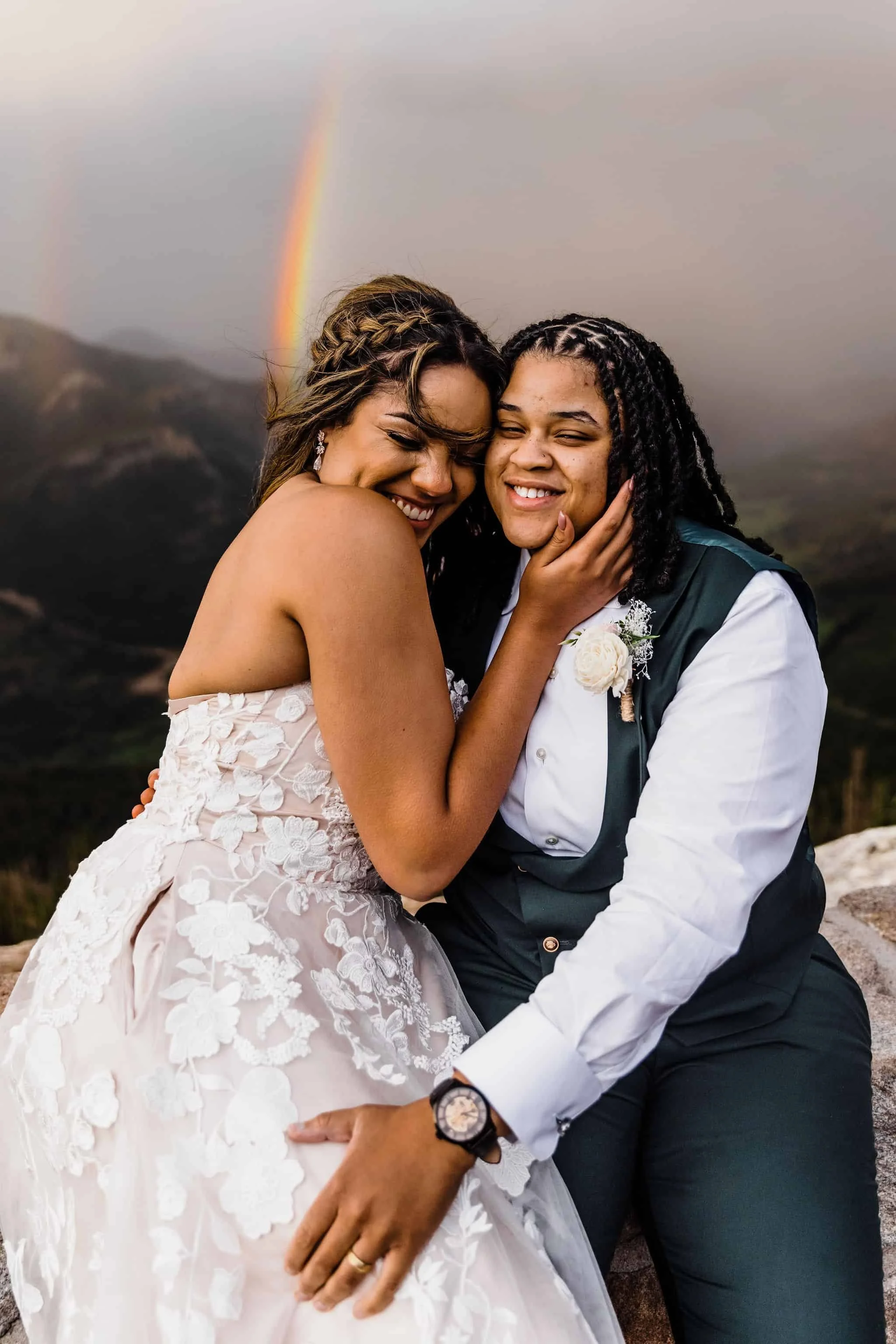 A couple snuggles together with a rainbow in the background