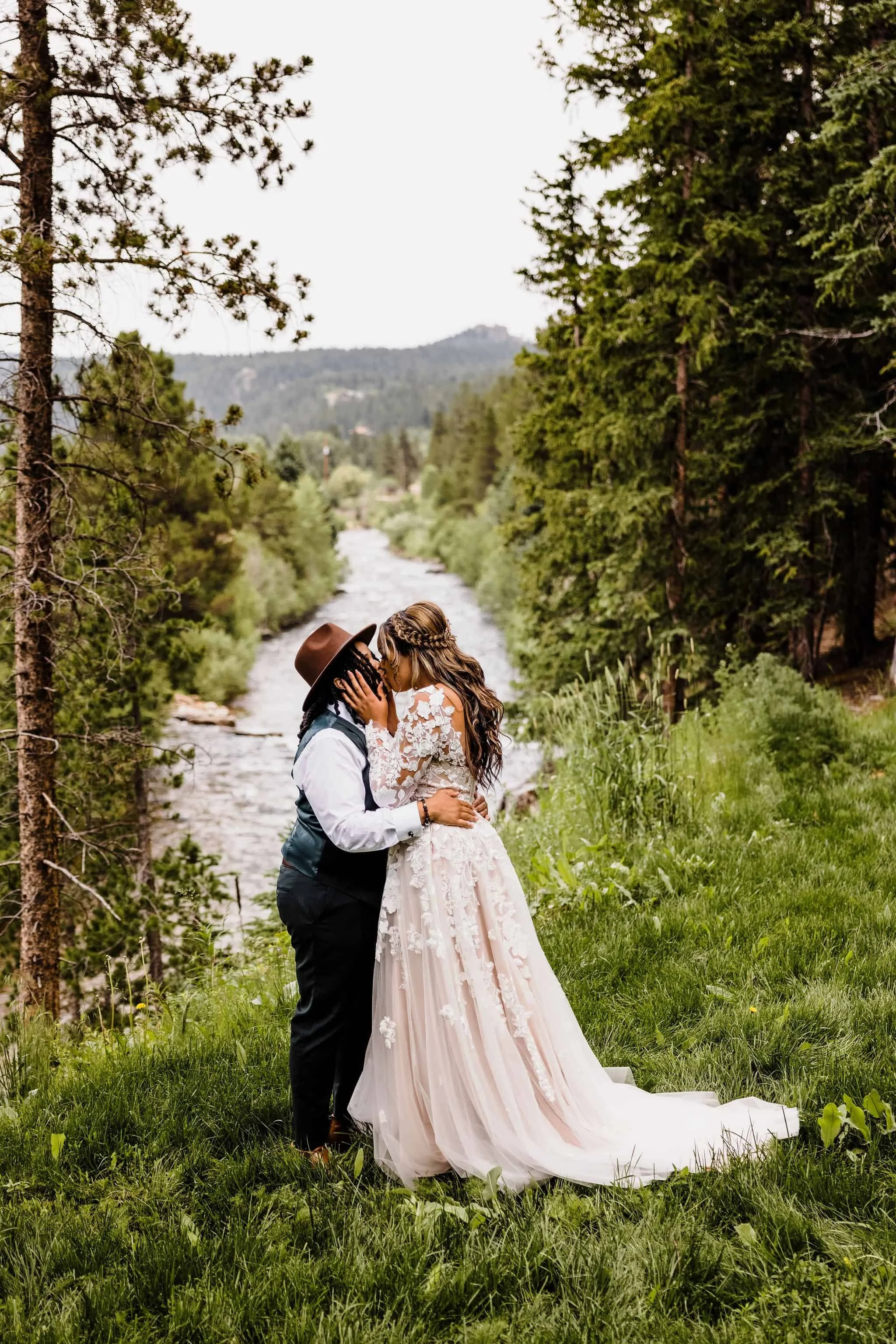 Two brides kiss next to a river