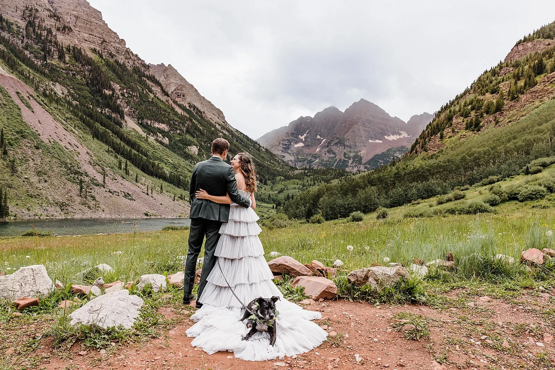 A couple stands at the Maroon Bells with their dog