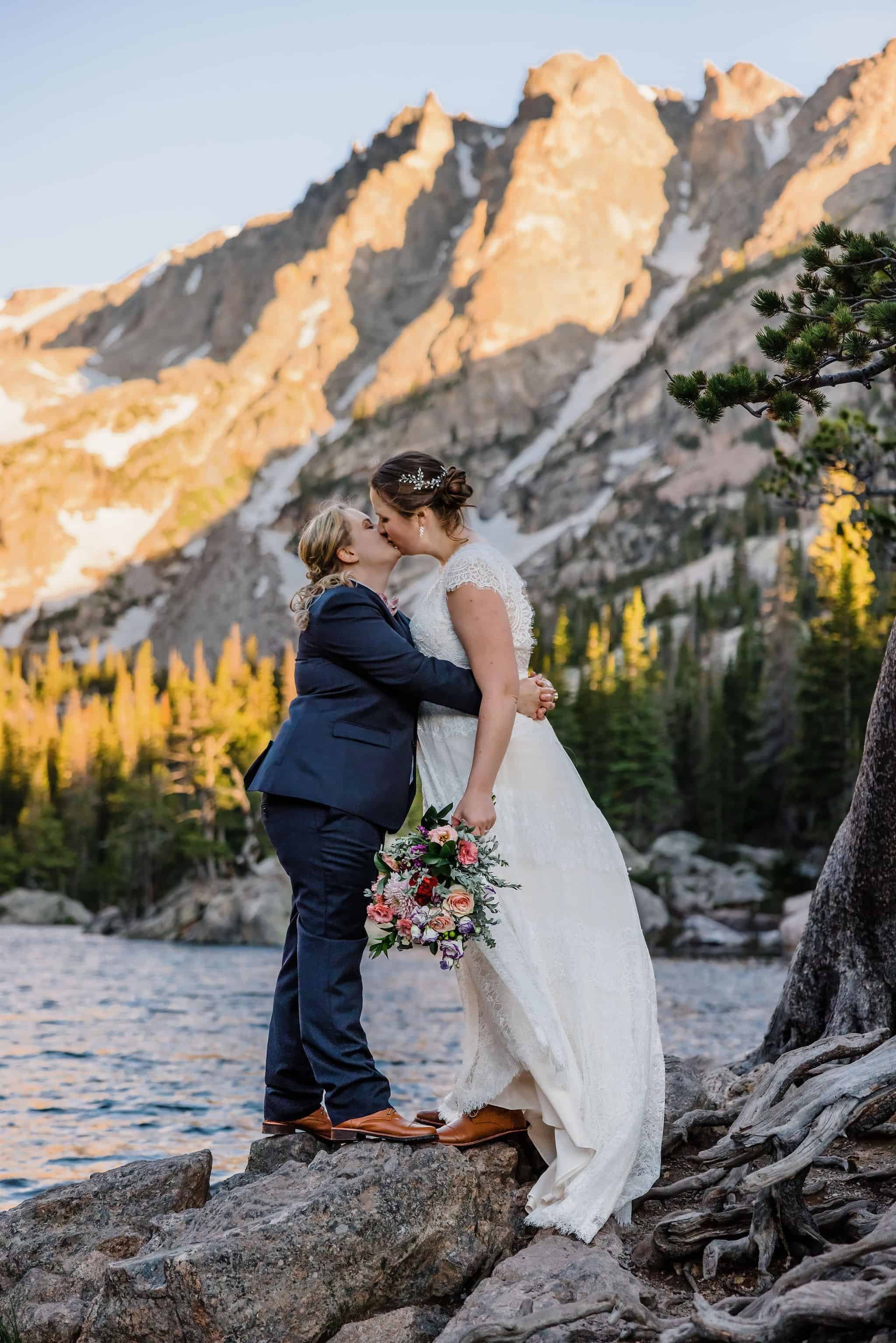 Two brides kiss next to an alpine lake