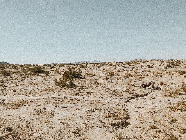 A person lying on their back in a desert landscape with sparse vegetation and mountains in the distance.