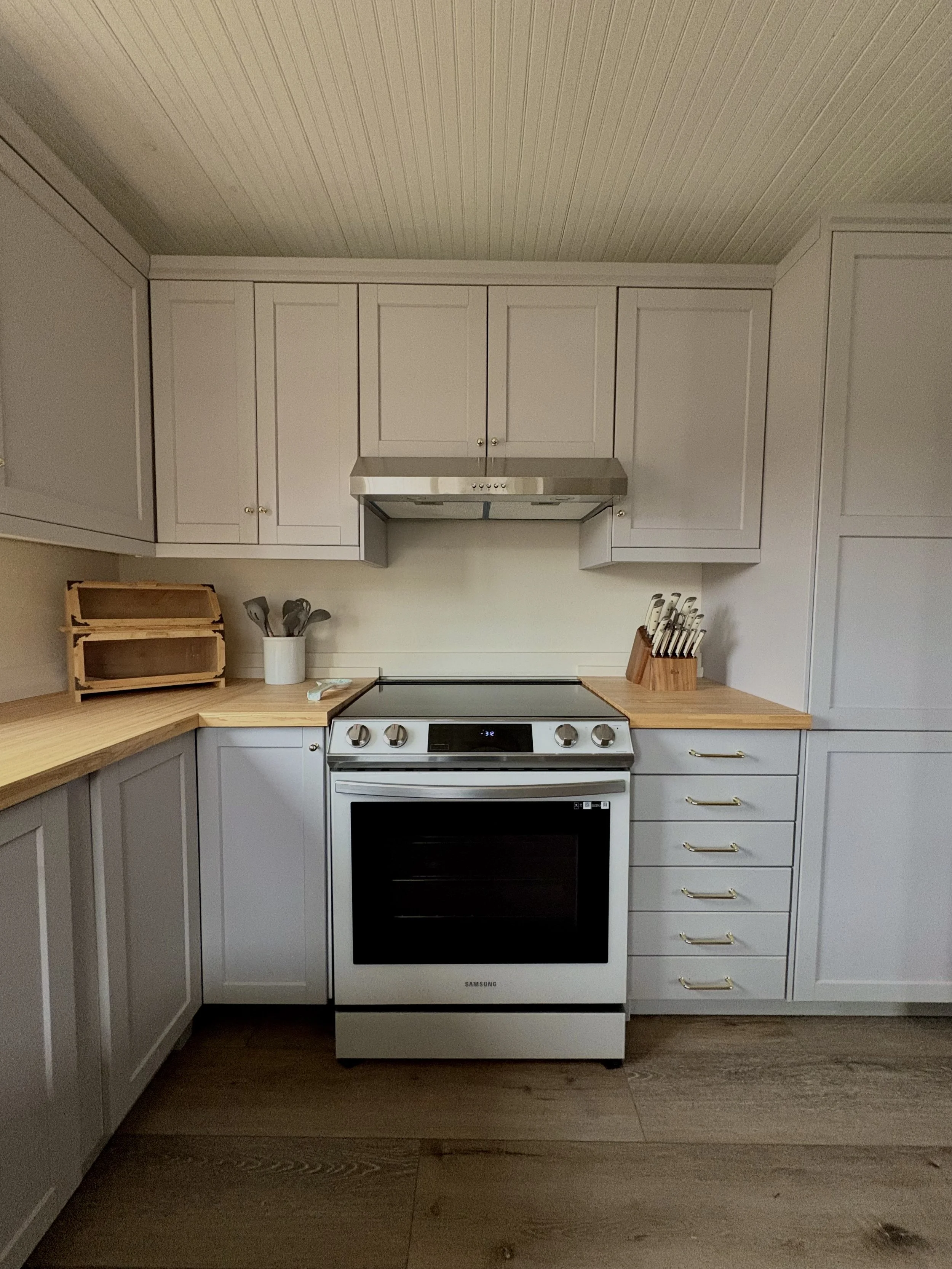 Kitchen with cabinet, stove, and wooden countertops, some utensils and knife set on the counters.