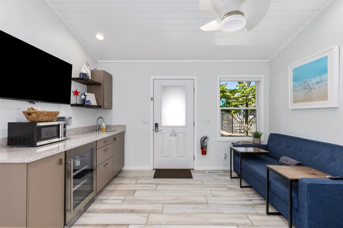 Small living area with kitchenette, blue couch, and a large window showing trees outside.