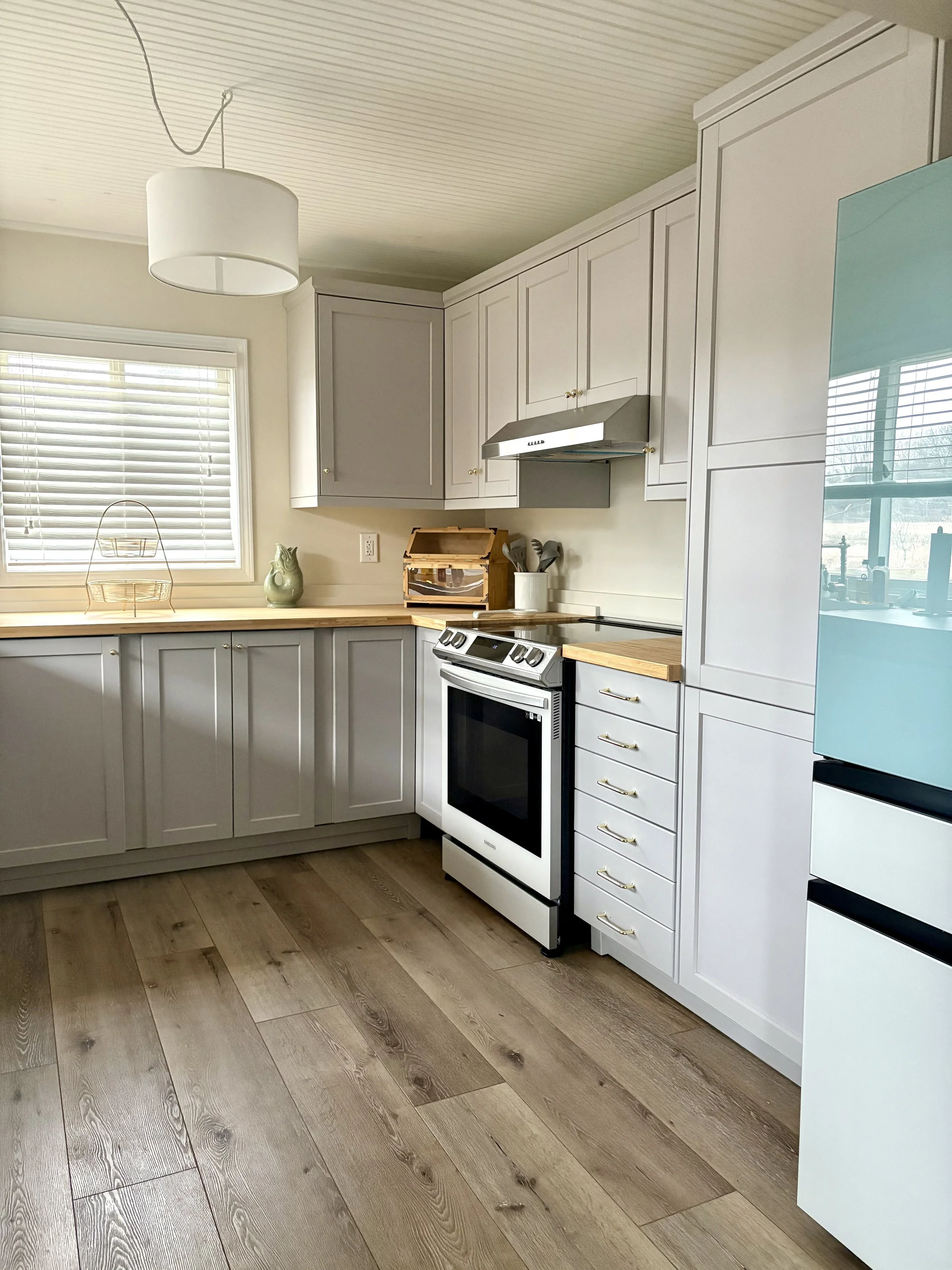 Kitchen with white cabinets, a window with blinds, a white stove, wooden countertops, and decorative items.