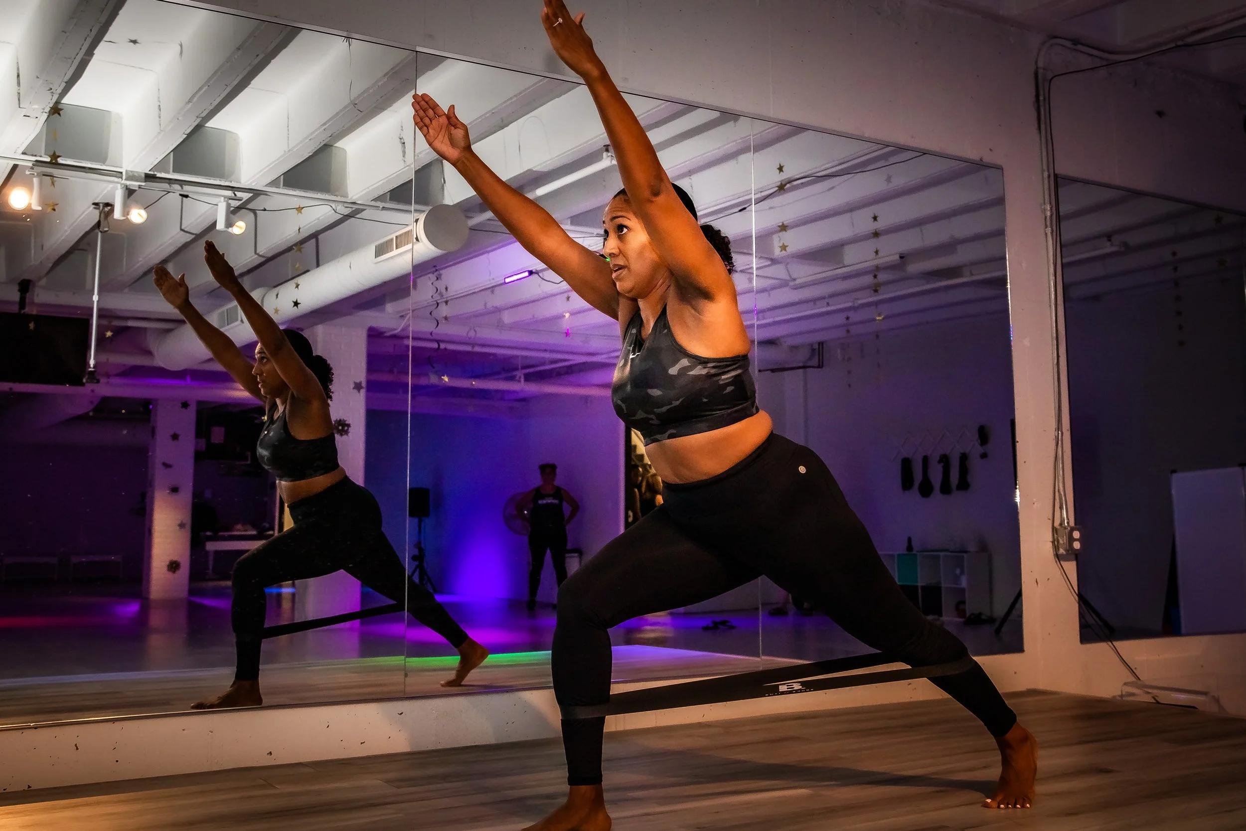 A woman performing a yoga pose in a studio with mirrored walls.