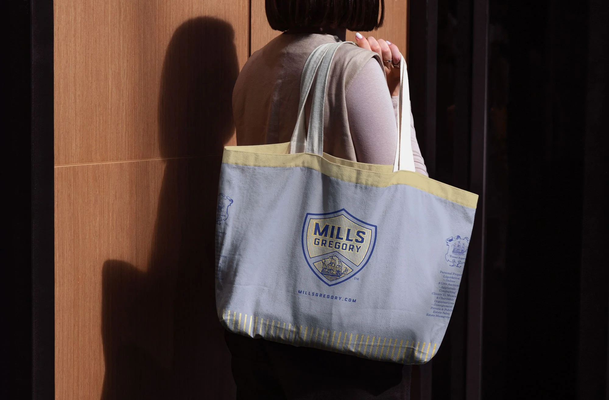 Woman with blue and gold branded cloth tote bag in front of interior with rich natural wood walls.