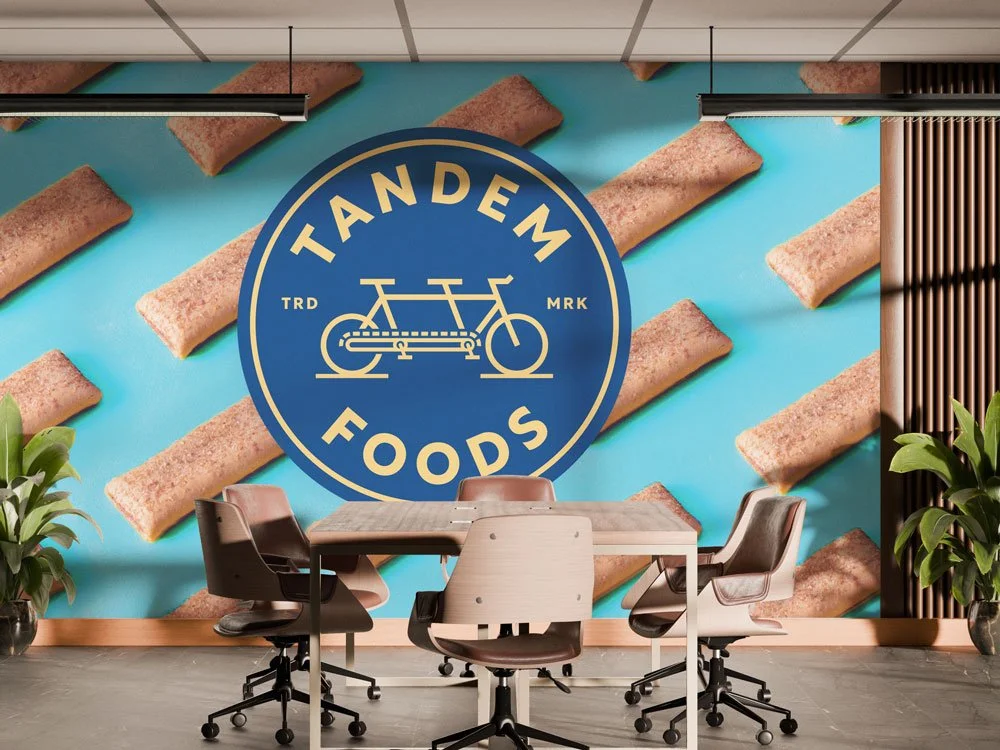 Office boardroom with graphic wall featuring blue and gold Tandem emblem over pattern of nutrition bars.