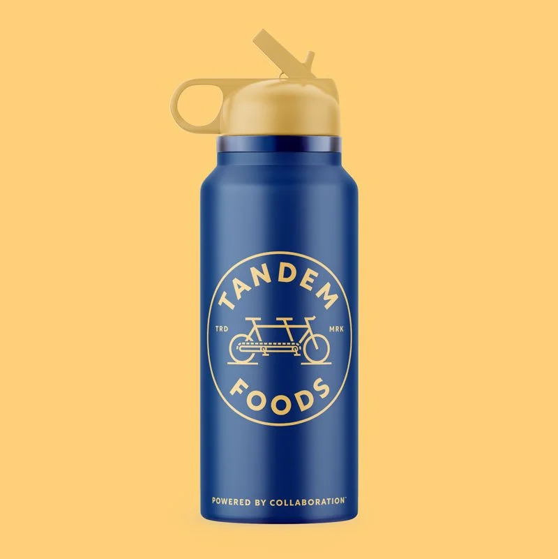 Blue water bottle with gold Tandem emblem and tagline. Bottle on gold background.
