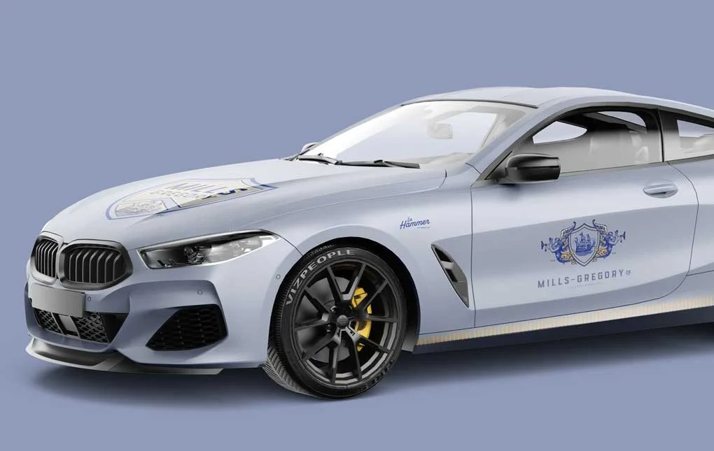 Mills-Gregory fleet sedan mockup with gold and blue graphic wrap over metallic light blue paint.
